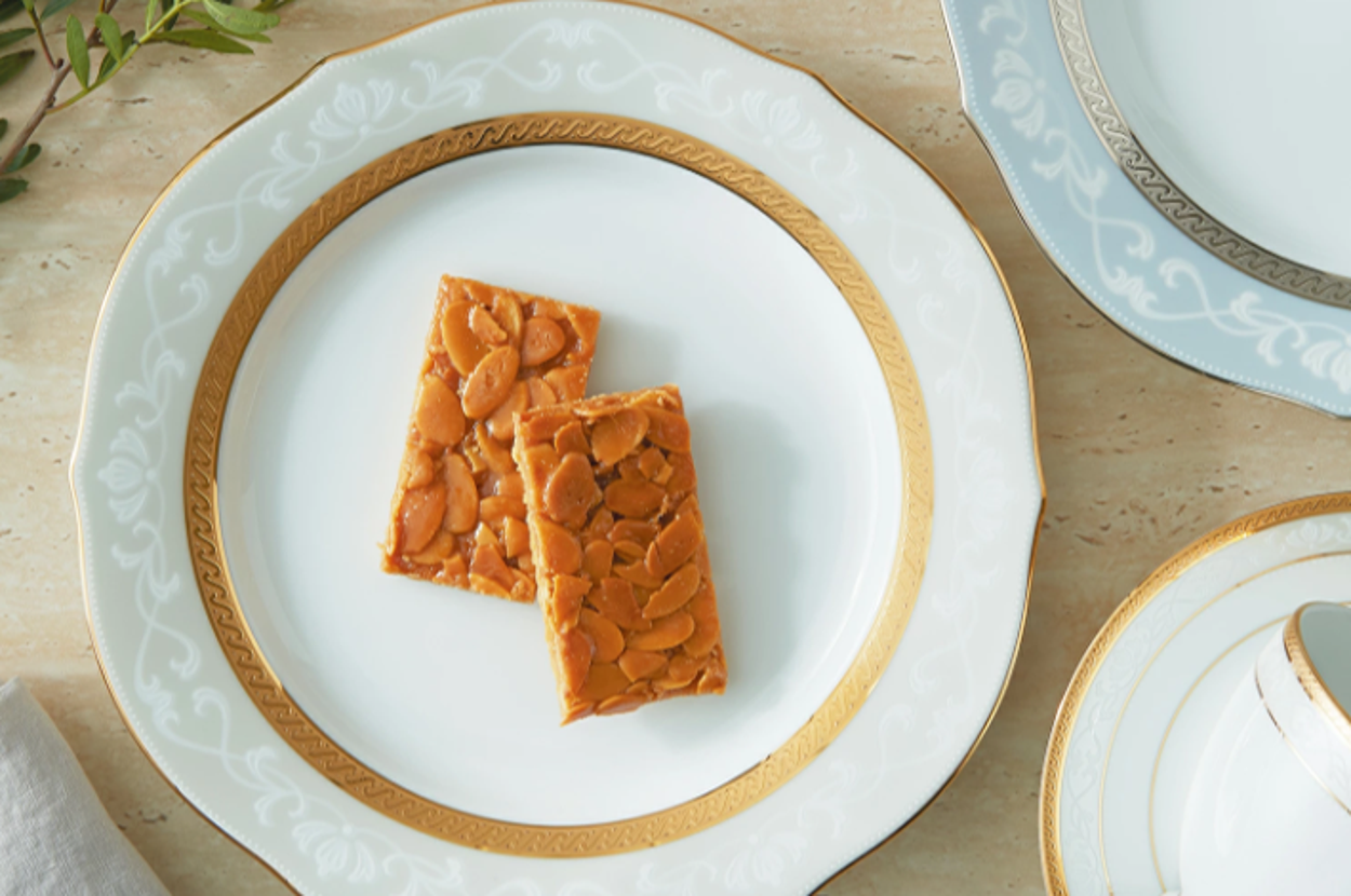 白い高級感のあるプレートにナッツの入った2枚のバーがのせられている。隣にティーカップと植物が飾られている。