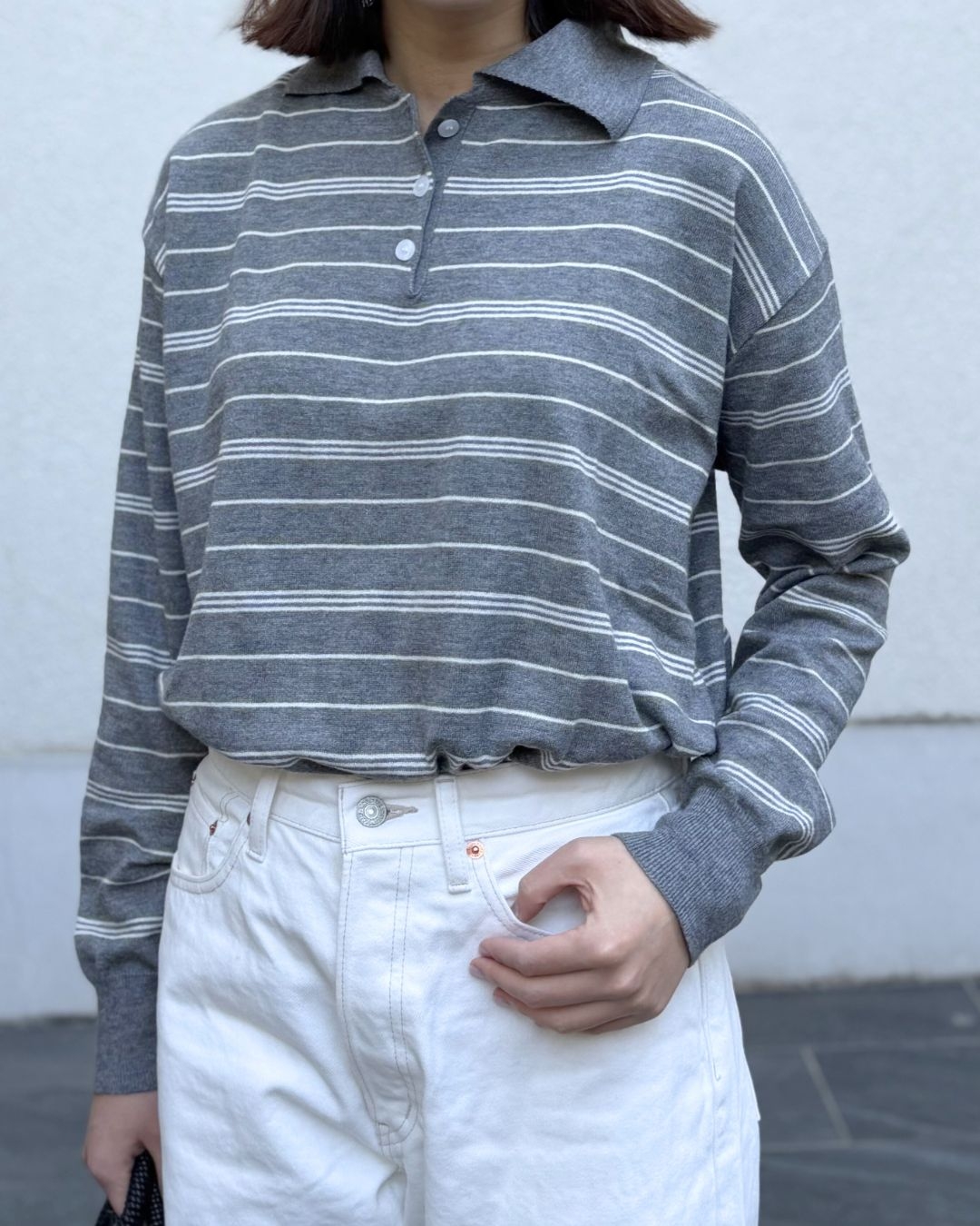 女性がストライプの襟付きシャツと白いパンツを着用。カジュアルでシンプルなスタイル。