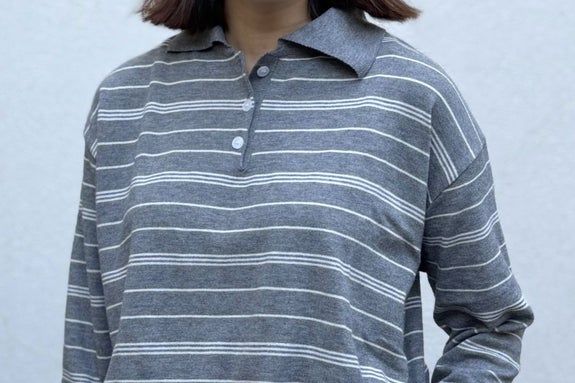 女性がストライプの襟付きシャツと白いパンツを着用。カジュアルでシンプルなスタイル。