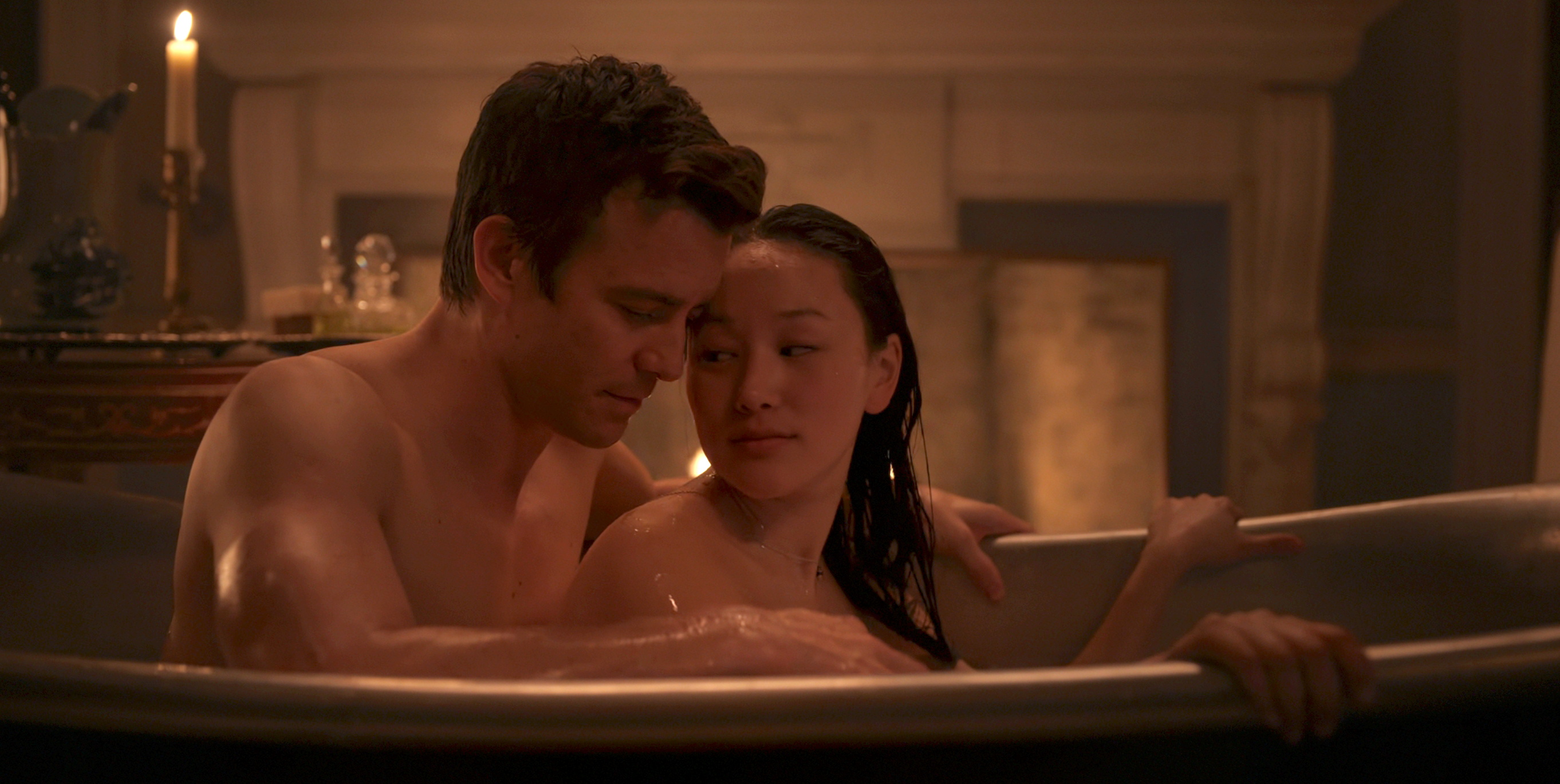 A man and woman share a tender moment in a candlelit bathtub, gazing into each other's eyes in an intimate setting