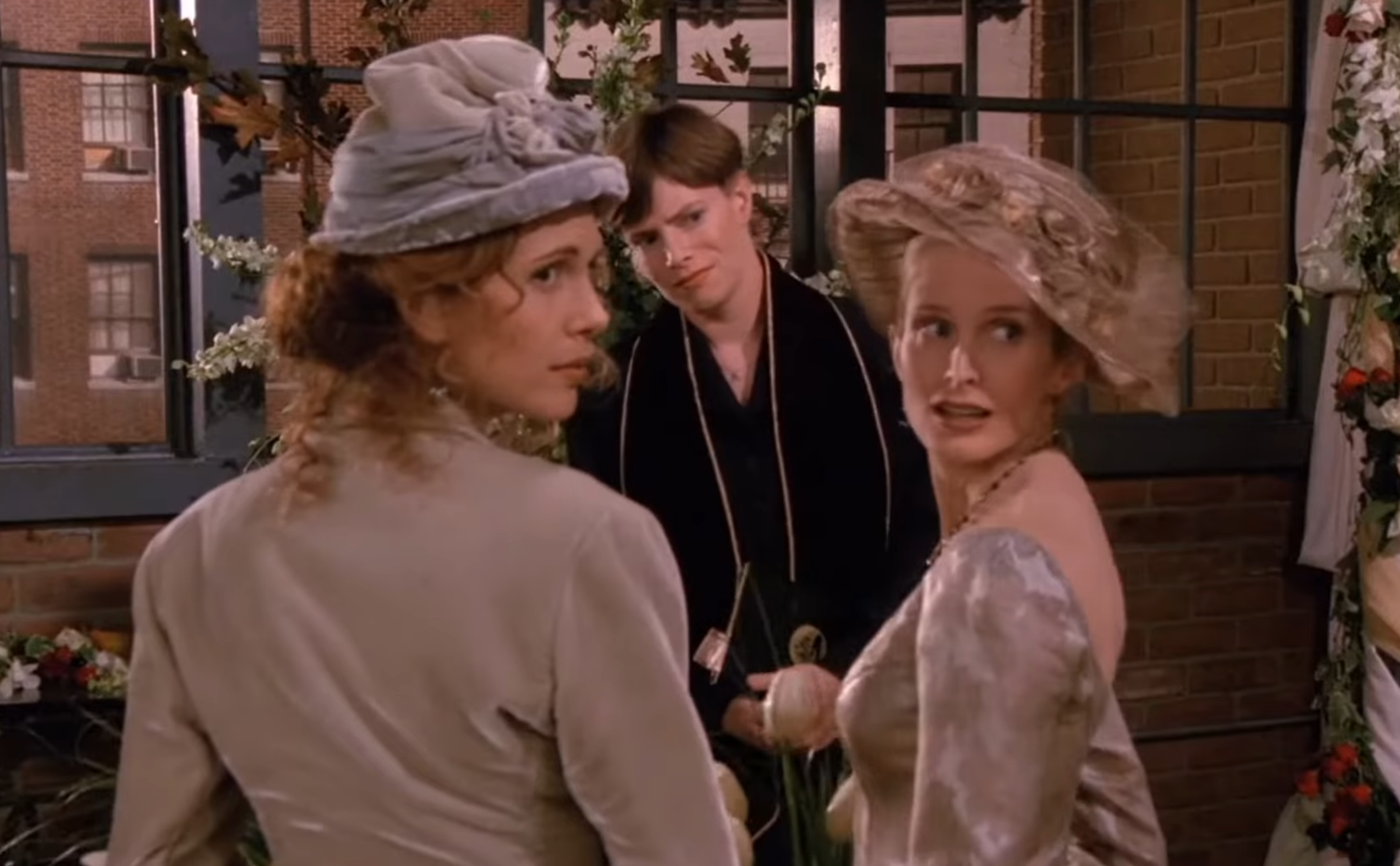 Three radical   successful  play  costumes with hats successful  an indoor setting. Two women look   each   other, a antheral   stands down  them with a funny  expression