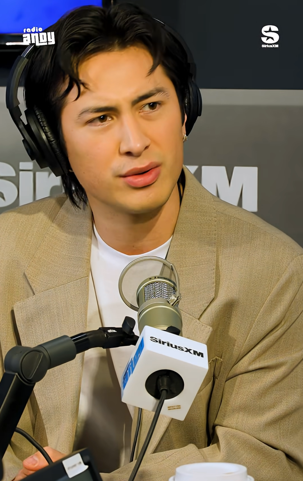 Person wearing headphones and a blazer speaks into a microphone successful  a SiriusXM workplace  setting