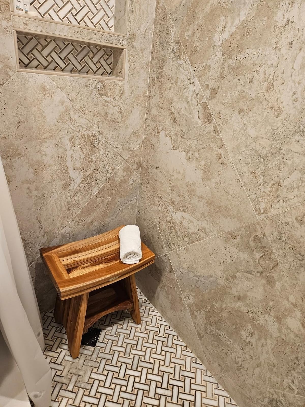 Wooden stool with a rolled towel in a tiled shower corner, featuring geometric wall and floor patterns