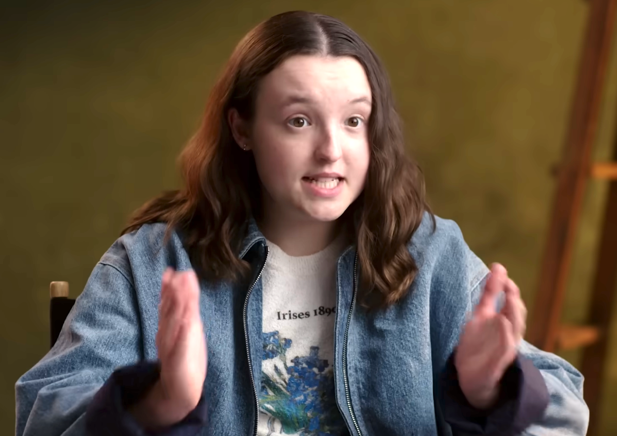 Person gesturing portion    speaking during an interview, wearing a denim overgarment   and floral people     shirt