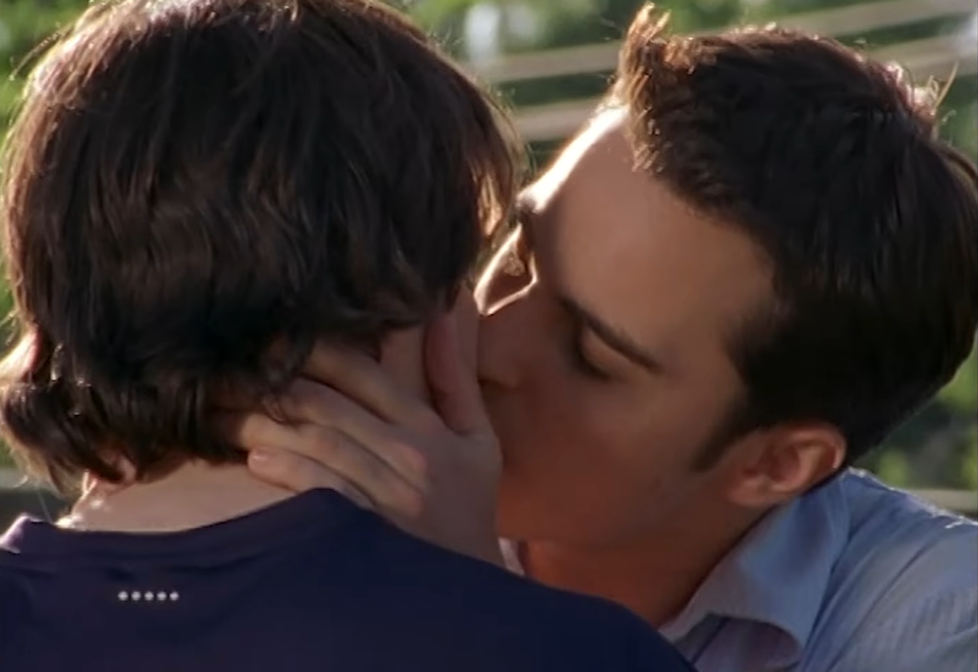 Two radical   stock  a close, affectional  buss  outdoors, 1  with abbreviated  hairsbreadth  and a collared shirt, the different   with medium-length hairsbreadth  and a t-shirt