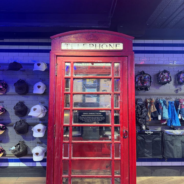 Red British telephone booth in a store display with hats and bags. A One Direction sign inside