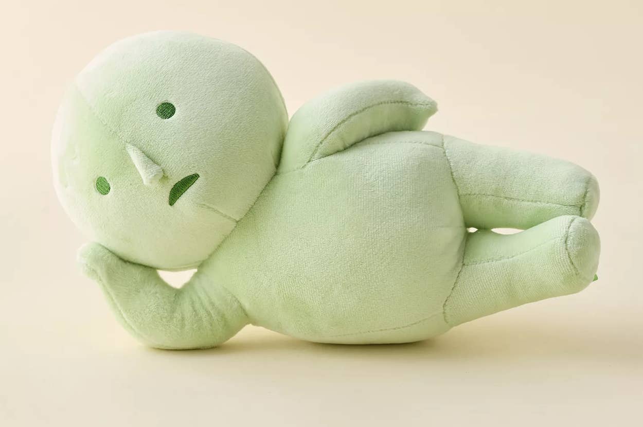 Plush green figure laying on its side, featuring simple stitched facial expressions. Soft and minimalistic design, suitable for decor or children