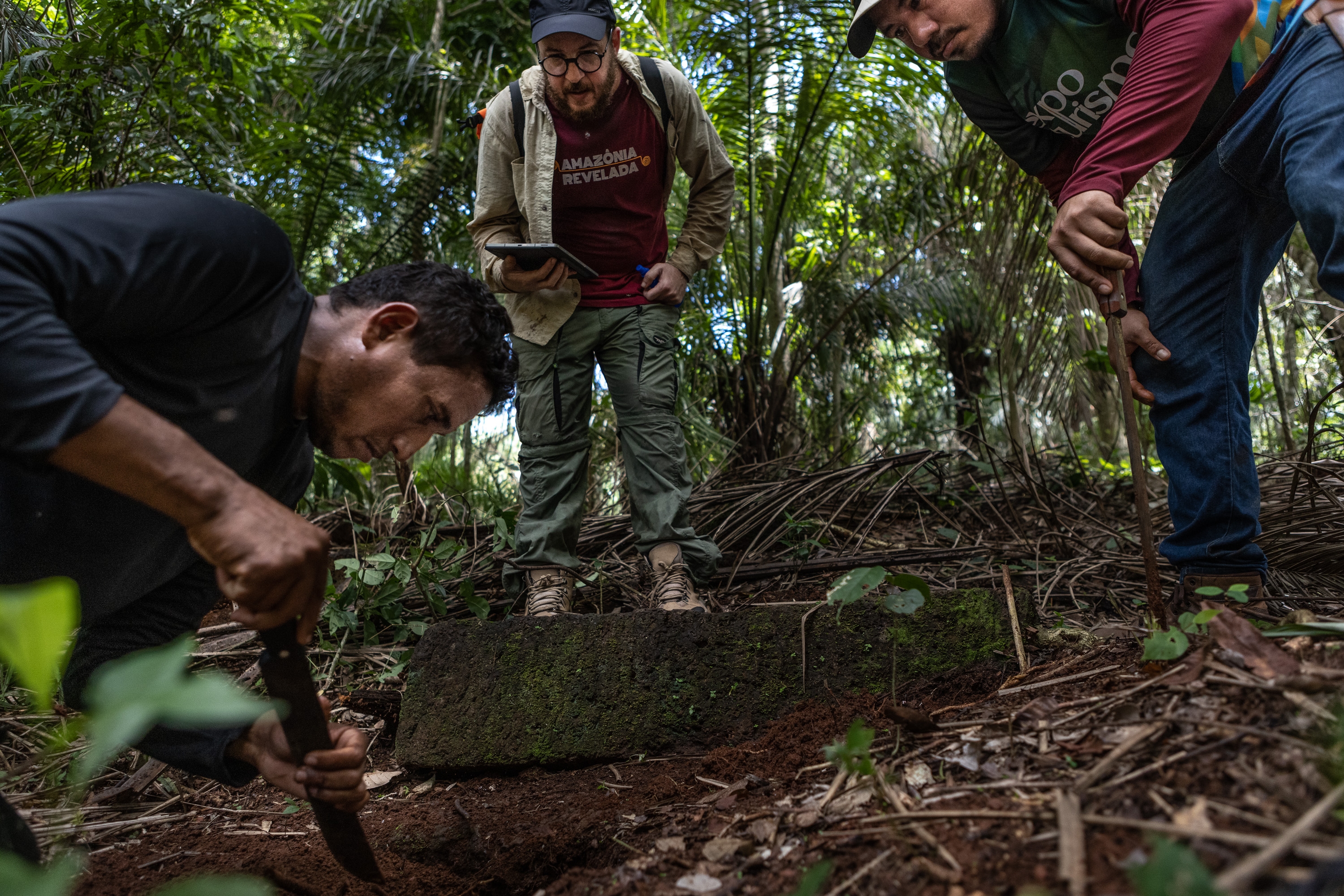 Three radical   excavate astatine  a tract  successful  a dense forest, utilizing tools to excavation  into the ground, observed by different  holding a notebook