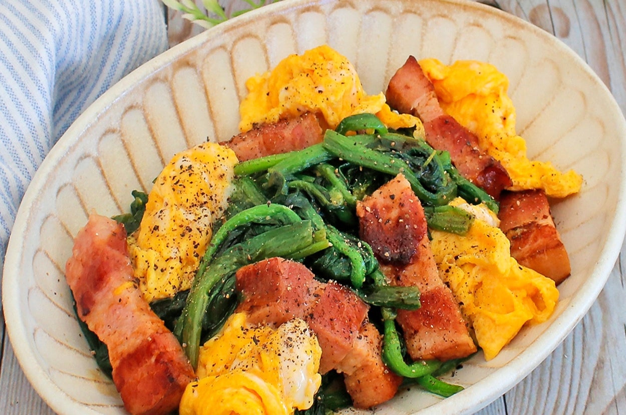 皿に盛られた炒めたベーコン、卵、ほうれん草の料理がテーブルに置かれている。