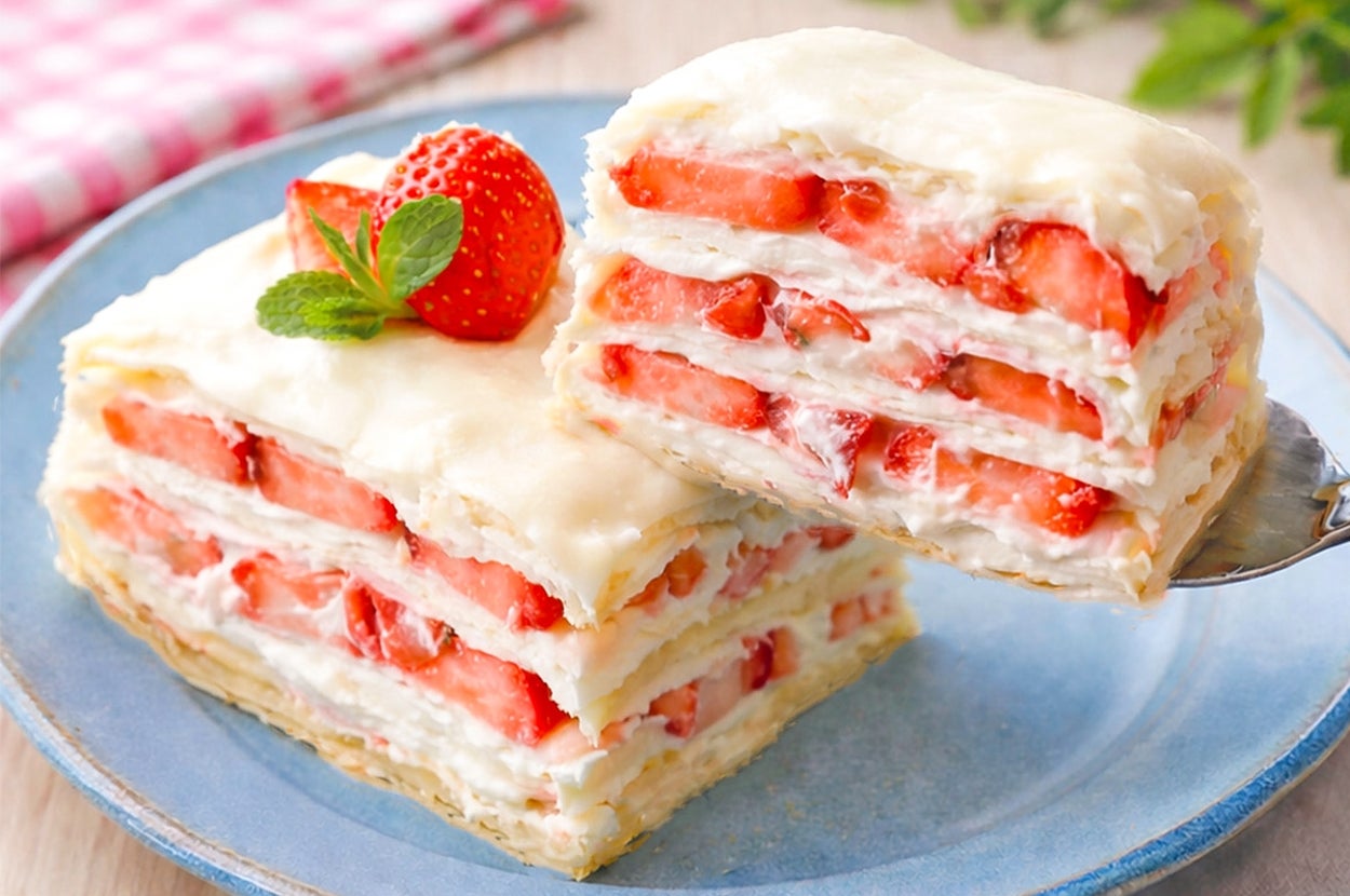 イチゴとクリームが層になったケーキが青い皿に盛られている。ケーキの一部がスプーンですくわれている。