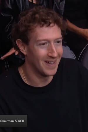 Mark Zuckerberg sitting in an audience, wearing a casual t shirt, smiling and watching an event