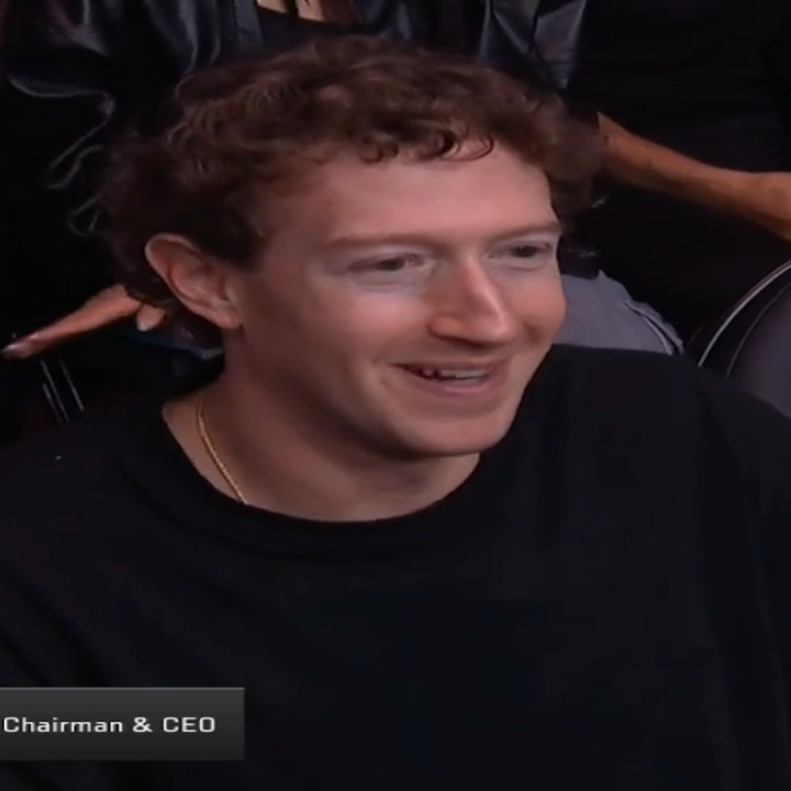 Mark Zuckerberg sitting in an audience, wearing a casual t shirt, smiling and watching an event