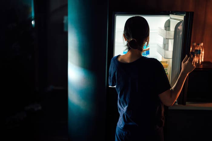 Person in casual clothing stands by an open fridge, looking inside