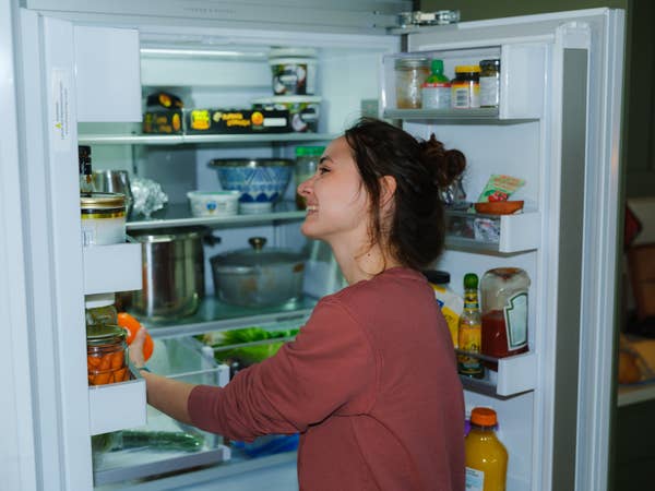 Person smiling while reaching into a stocked refrigerator
