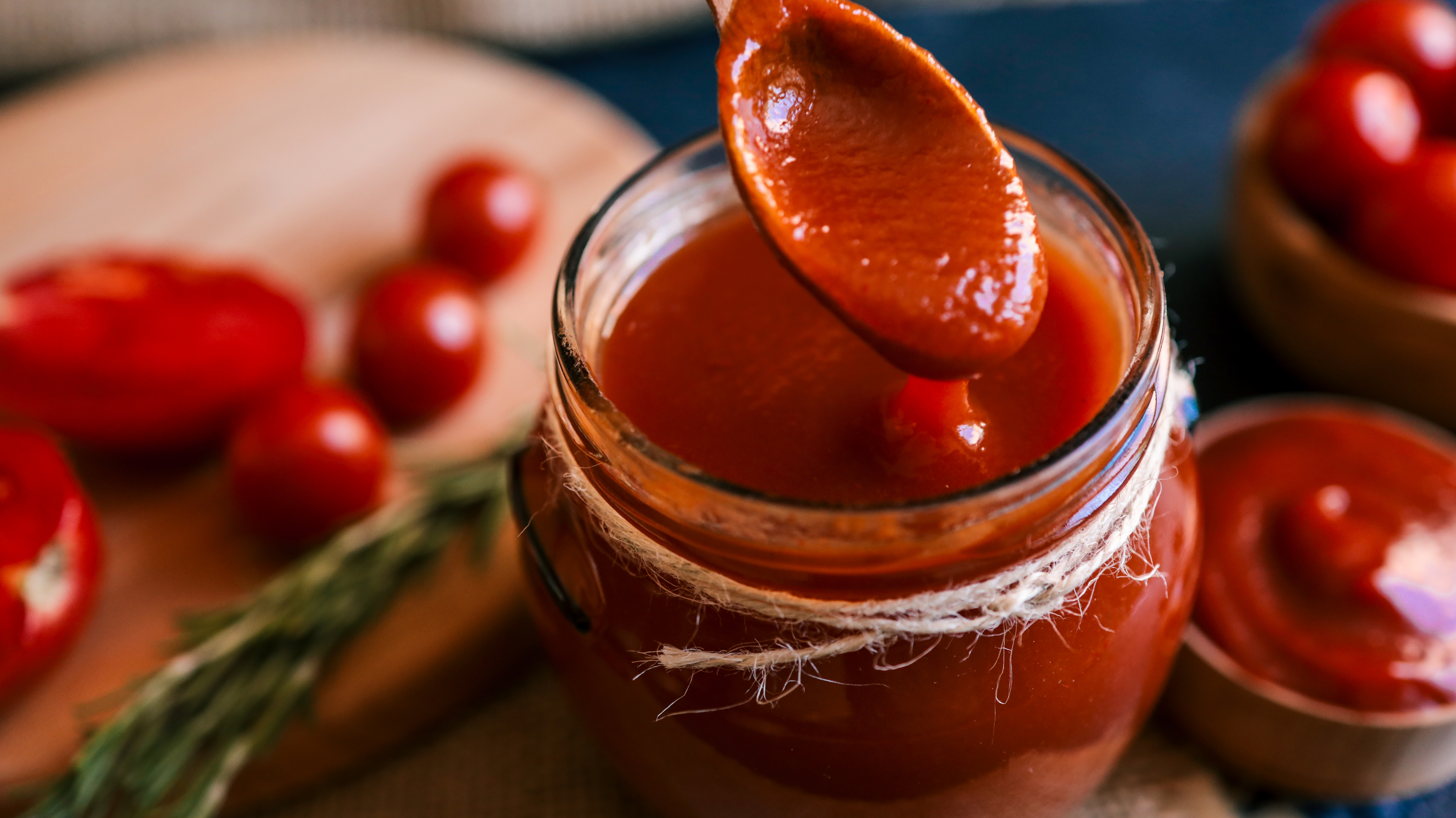 A jar of herb condiment with a spoon dipped successful it, surrounded by caller tomatoes and a sprig of rosemary connected a woody board