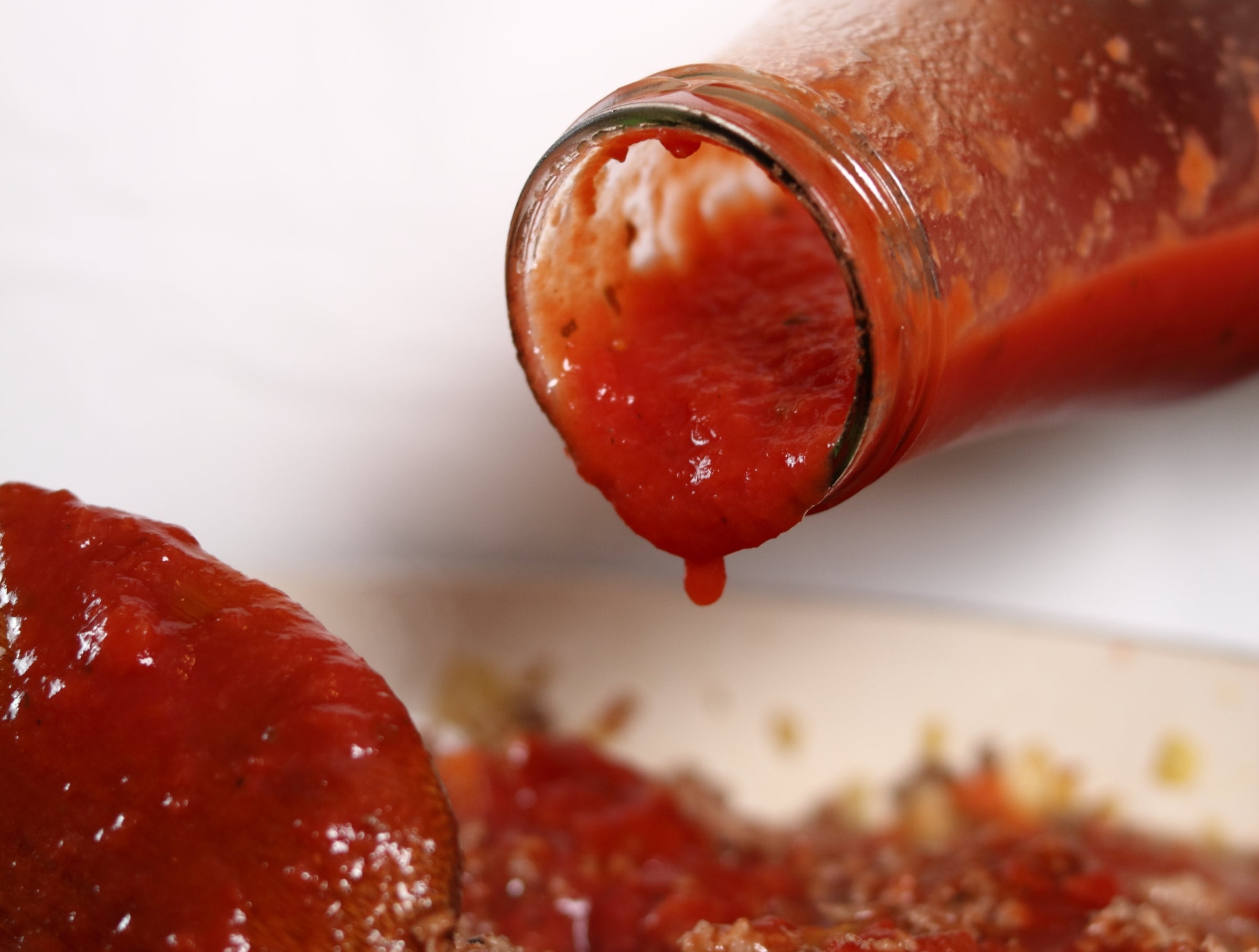 Spaghetti condiment being poured from a solid vessel into a cookware of cooked crushed meat, highlighting a cooking process