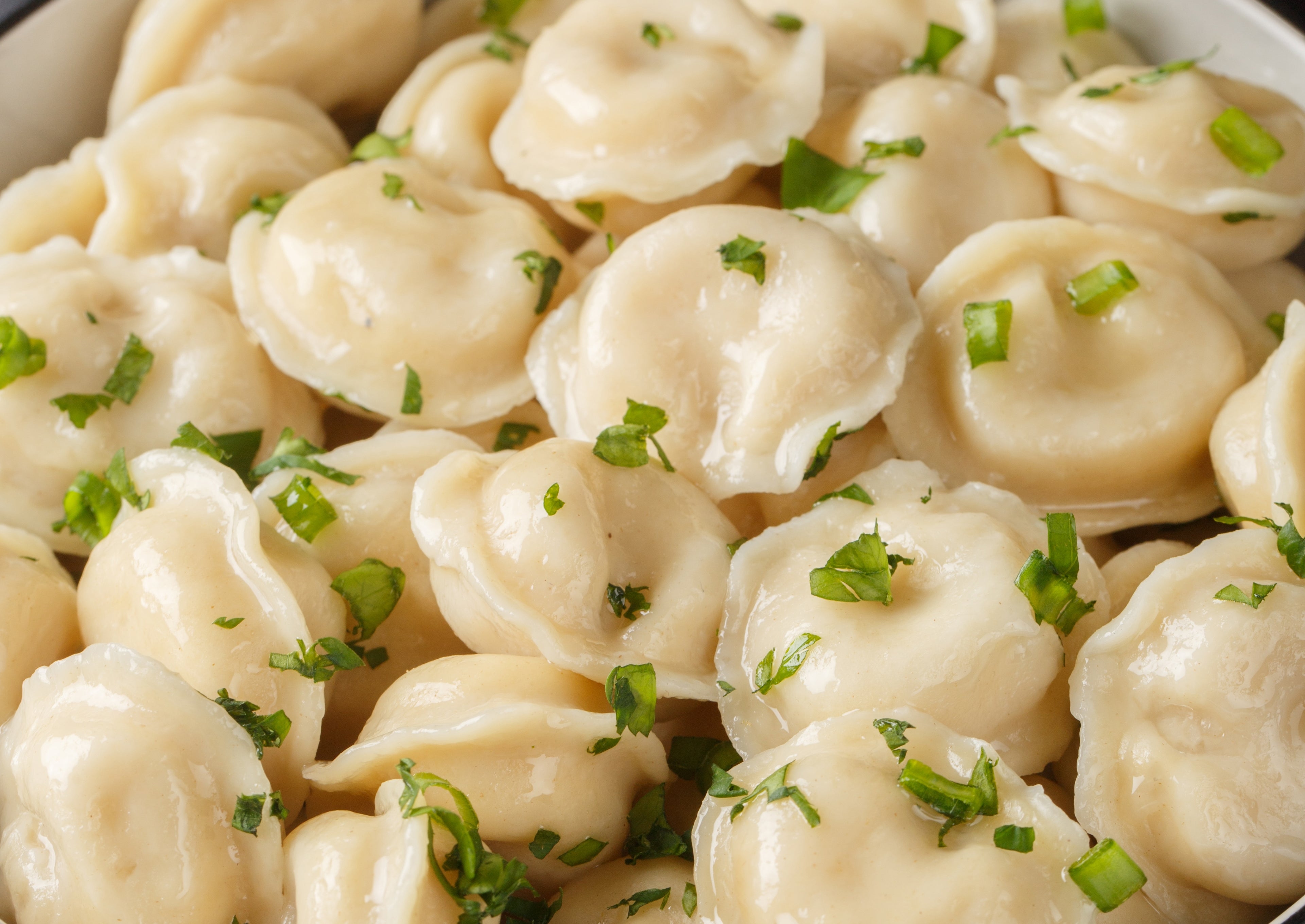 A vessel of dumplings garnished with chopped herbs, accompanied by bowls of sour pick and food cubes