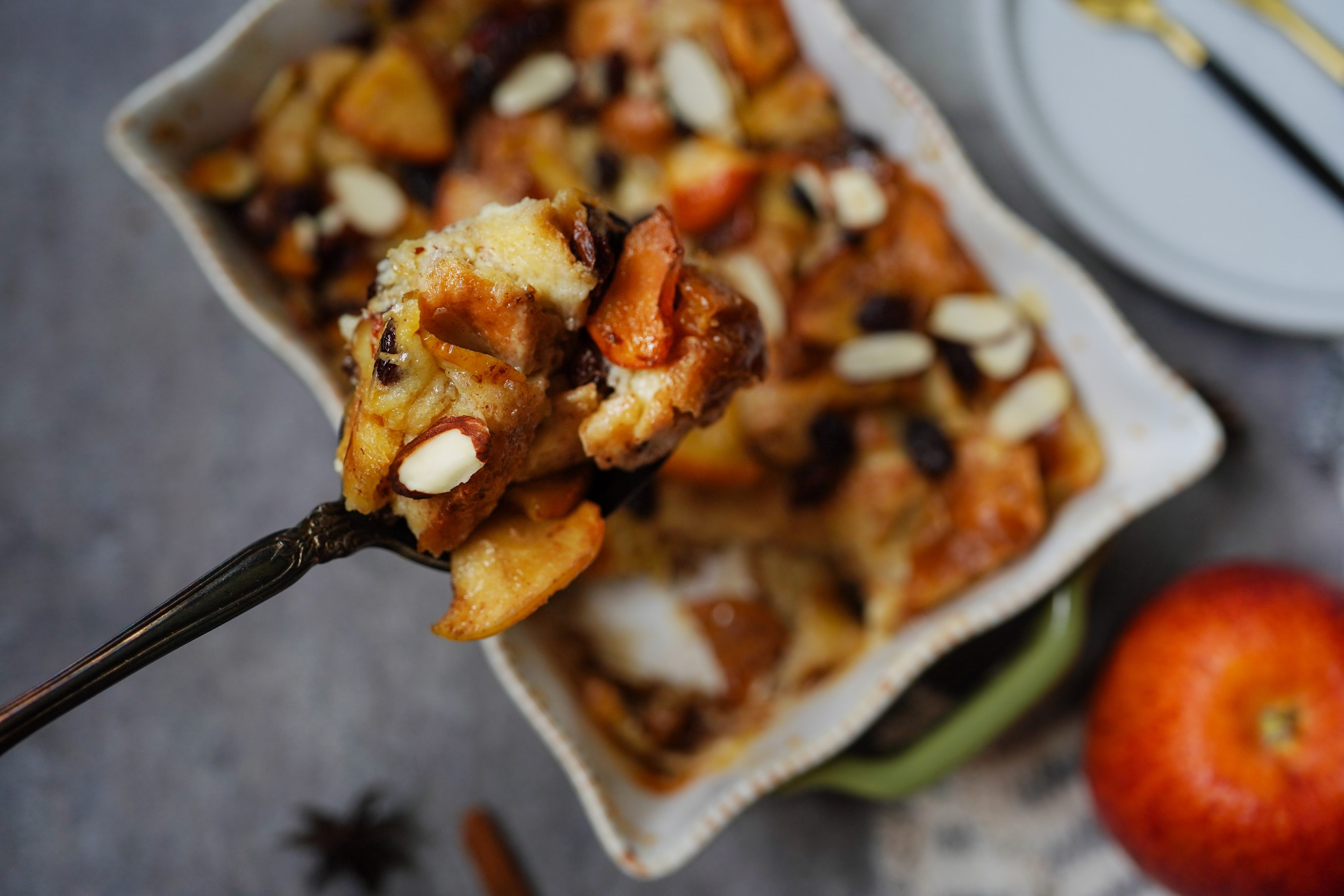 A spoonful of breadstuff pudding with almonds and fruit, held implicit a dish, with an pome nearby
