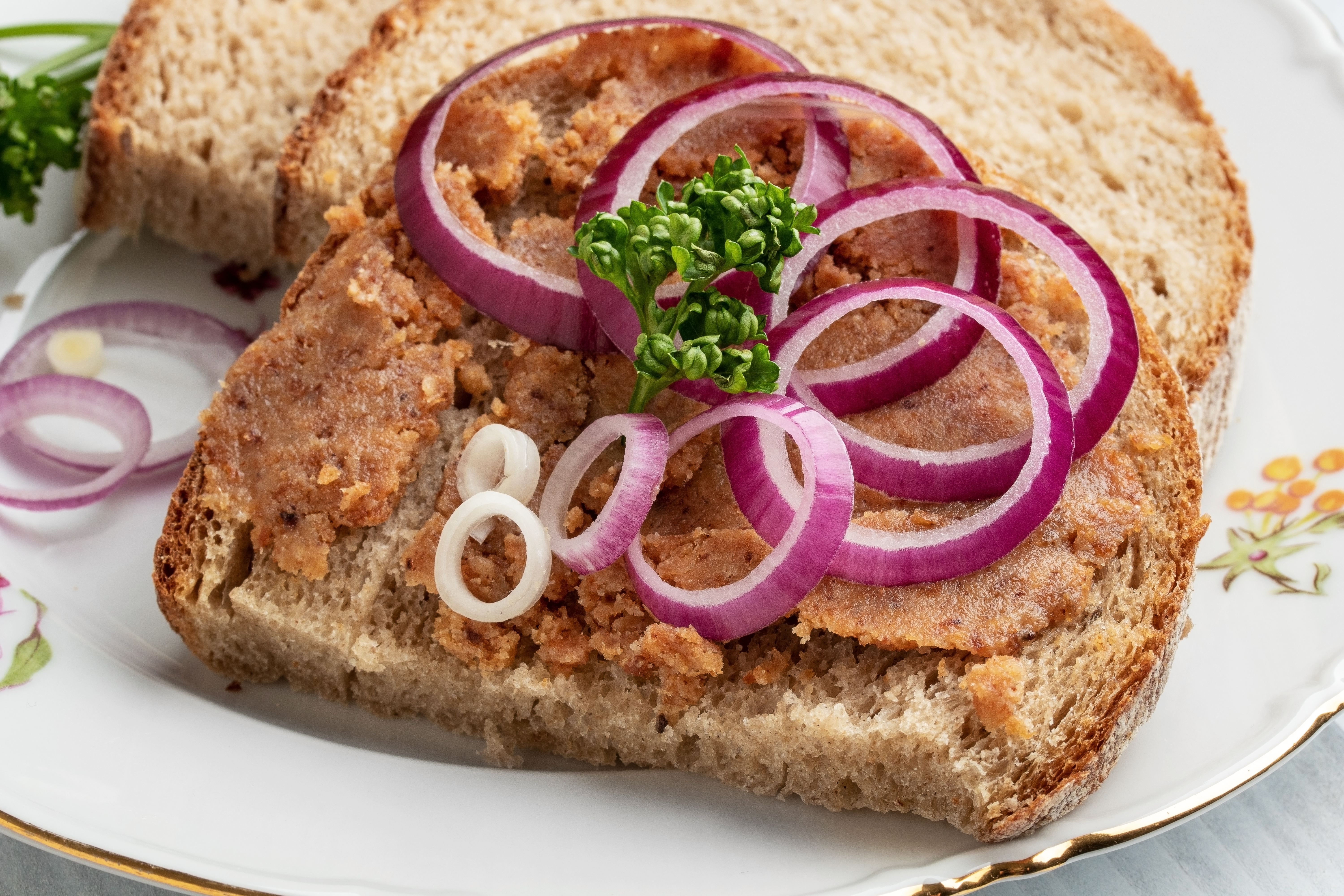 Open-faced sandwich with spread, topped with sliced reddish onions and parsley, served connected a patterned plate