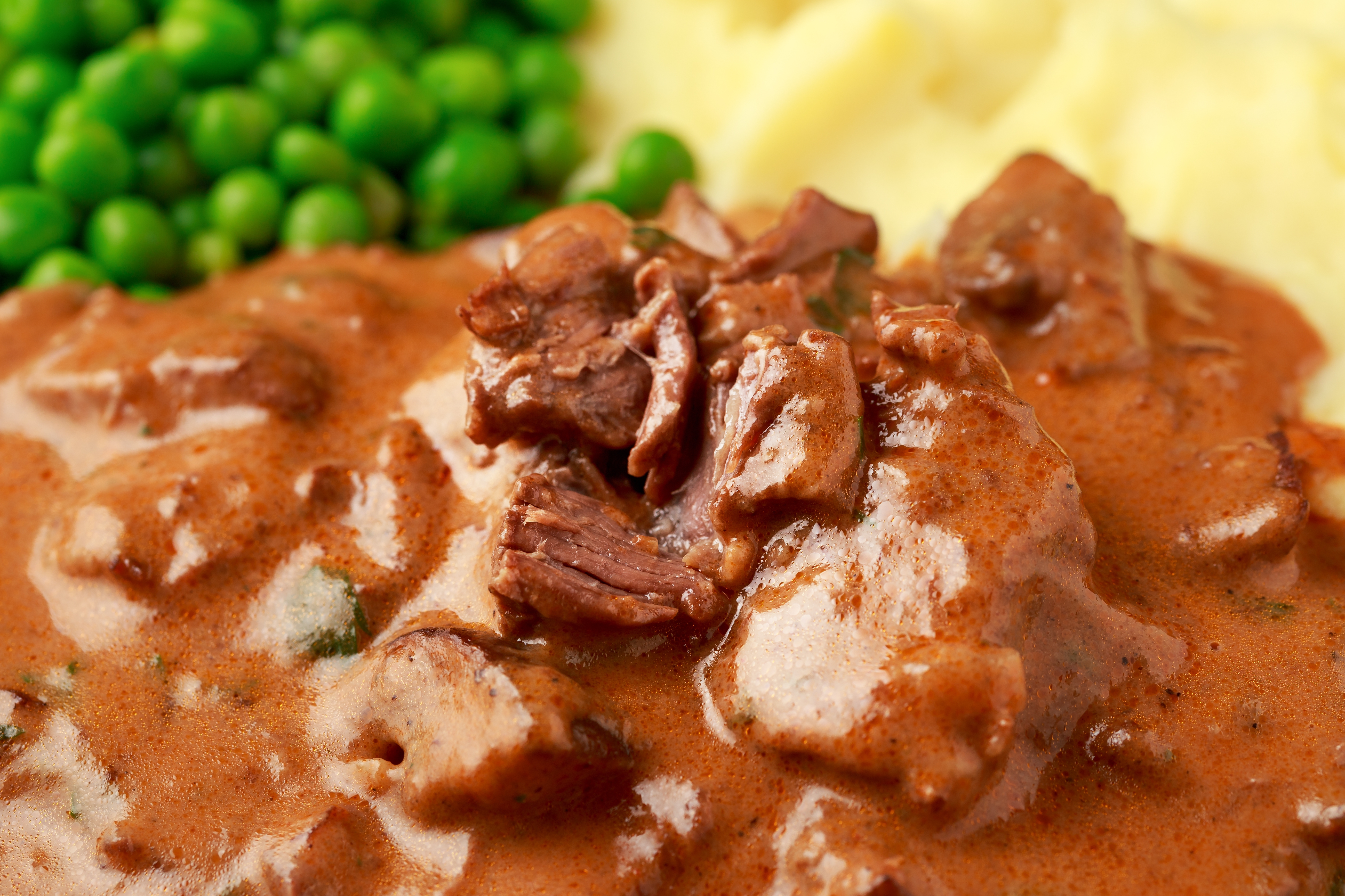 Close-up of beef stew with affluent sauce, mashed potatoes, and greenish peas