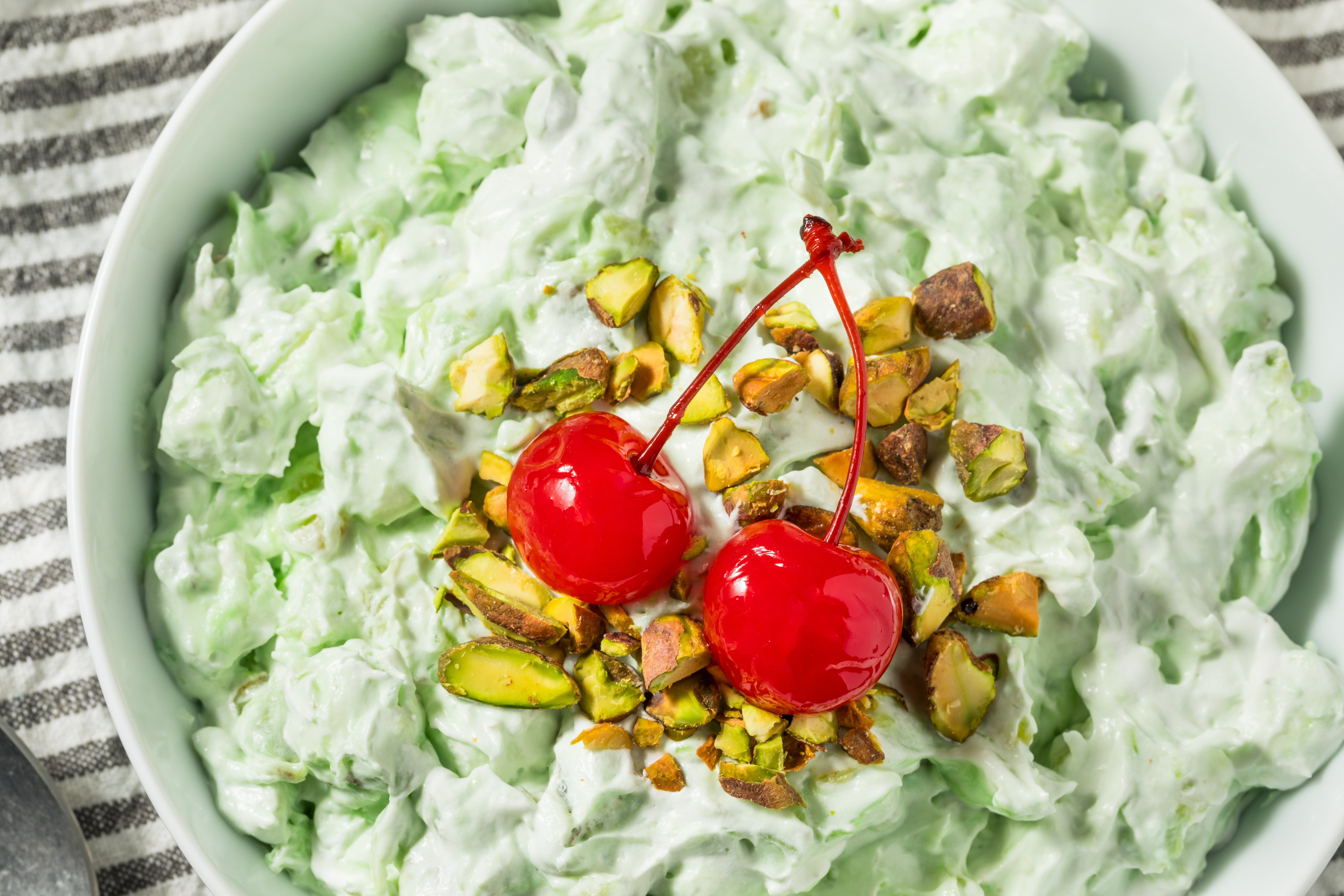 Bowl of mixed effect crockery with whipped cream, topped with pistachios and cherries