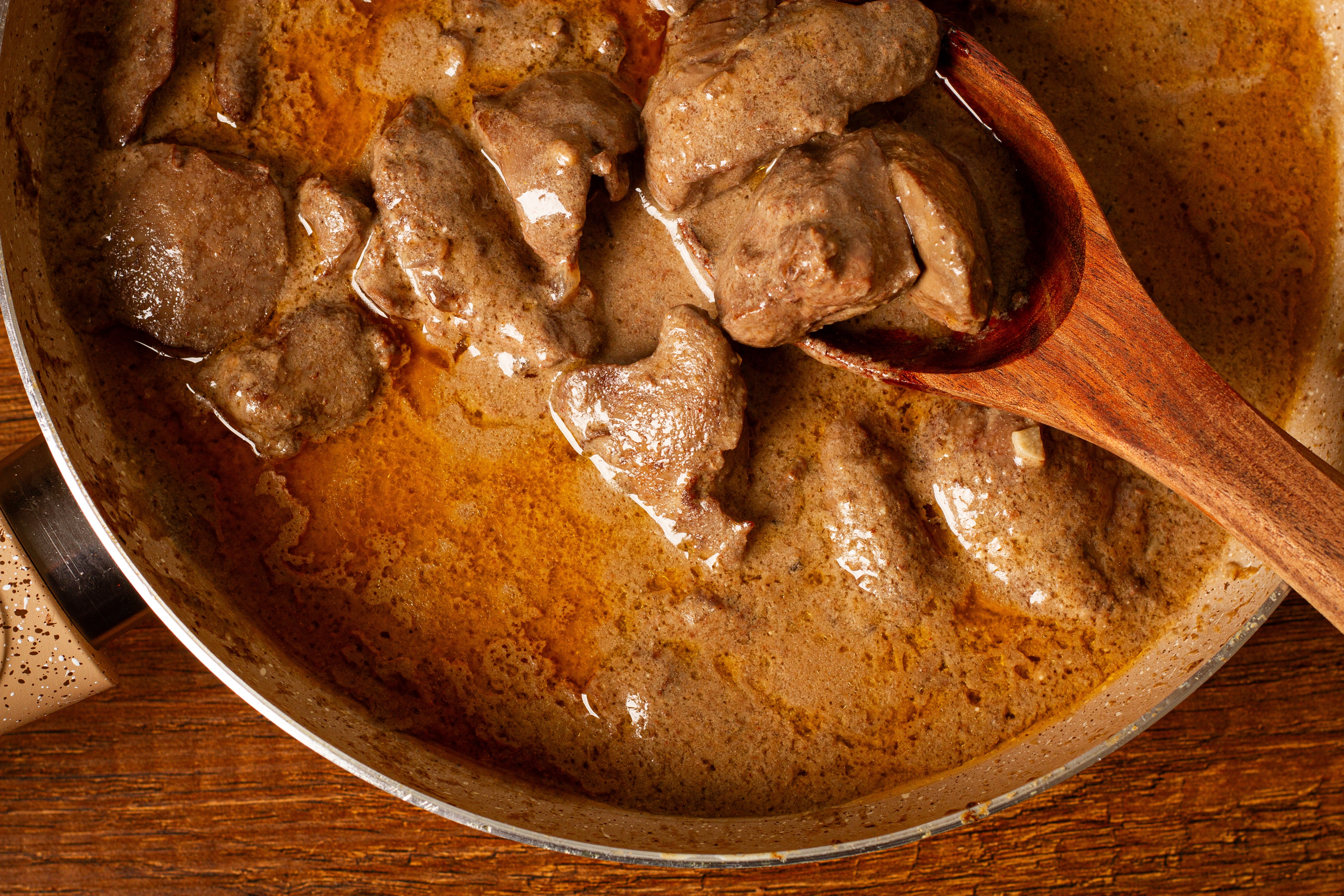Close-up of cooked liver pieces successful a creamy condiment successful a cookware with a woody spoon