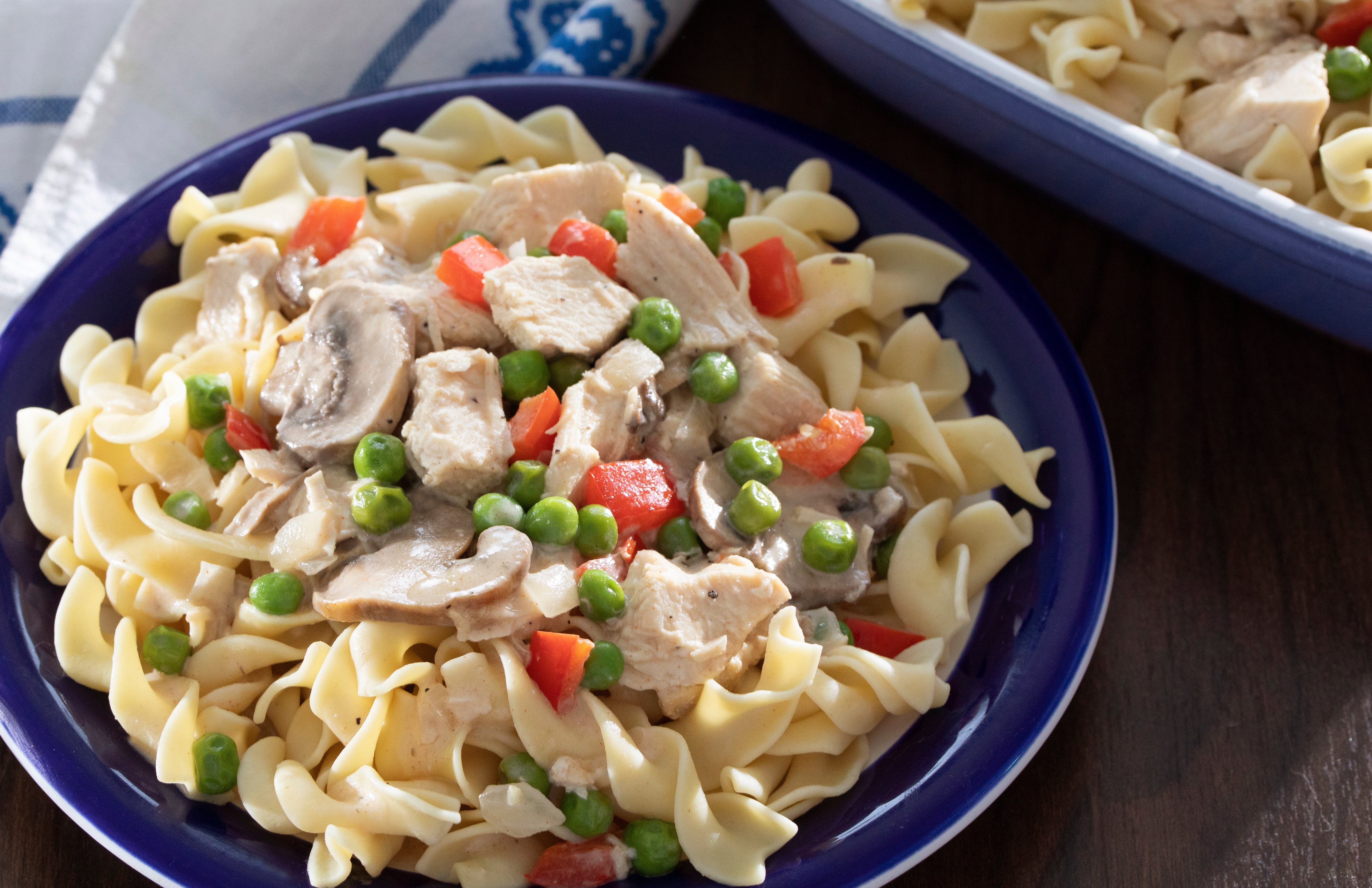 A sheet of pasta topped with creamy chicken, mushrooms, peas, and reddish peppers, served connected a woody array adjacent to a patterned napkin