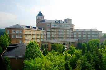 緑豊かな環境に立つ大きなホテルの外観。木々と空が広がる風景。