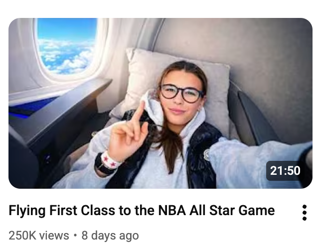 Person successful  an airplane's first-class spot   taking a selfie, wearing glasses and casual clothing. Text mentions flying to the NBA All-Star Game