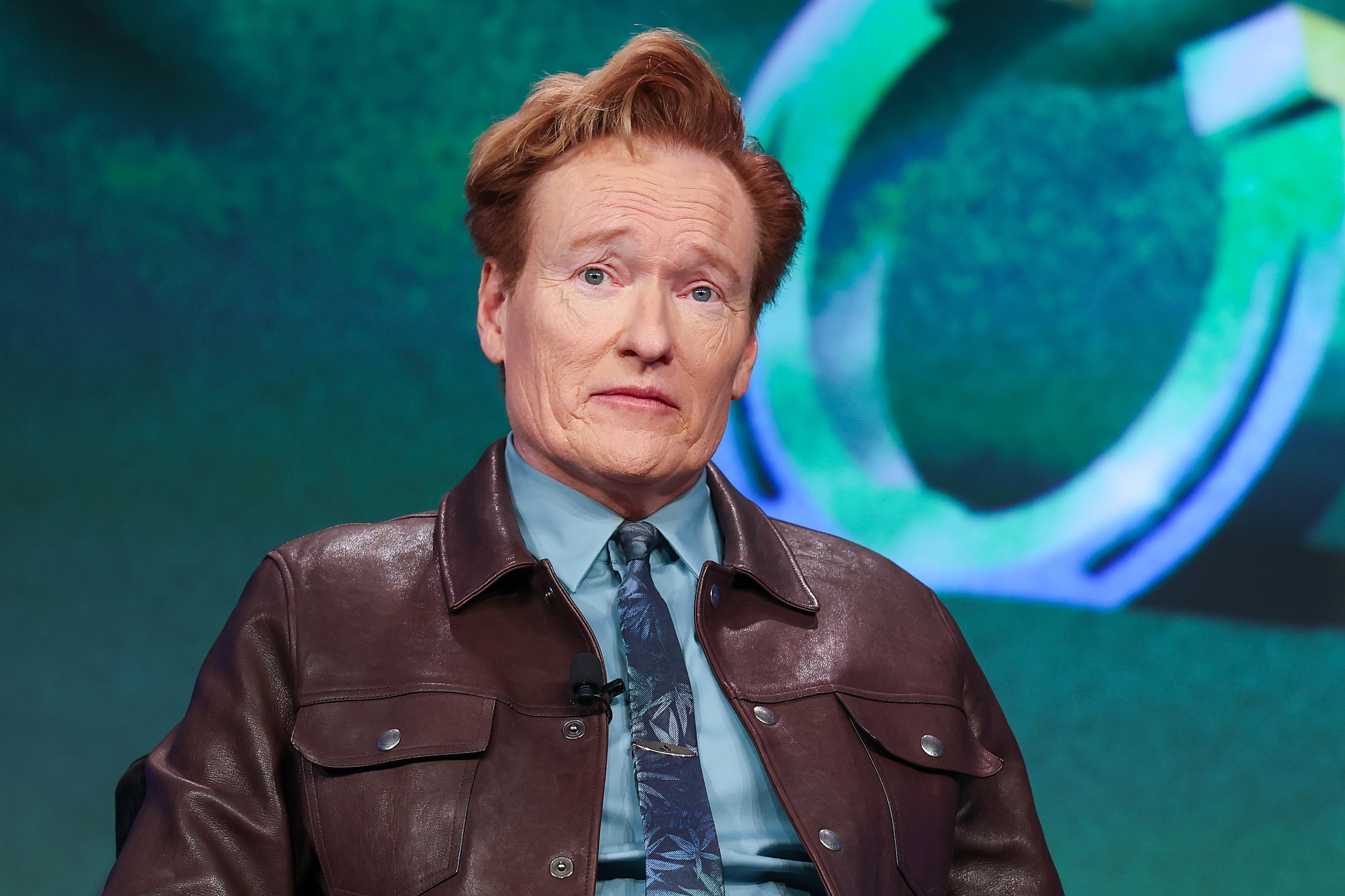 A idiosyncratic   successful  a leather overgarment   and necktie  is seated, looking somewhat  to the side