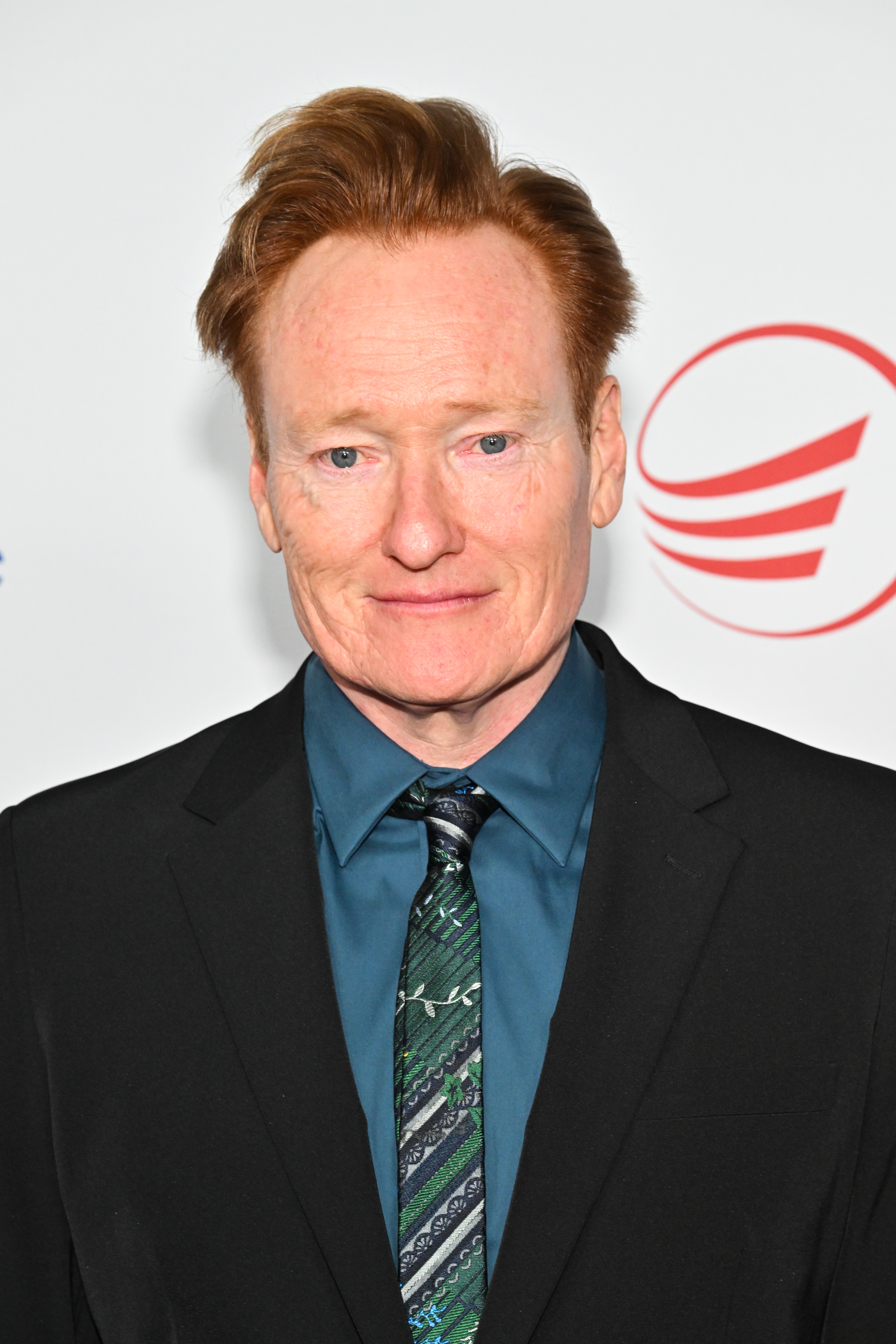 A idiosyncratic   connected  a reddish  carpet successful  a acheronian  suit   and patterned tie, posed against a backdrop with elemental  graphics