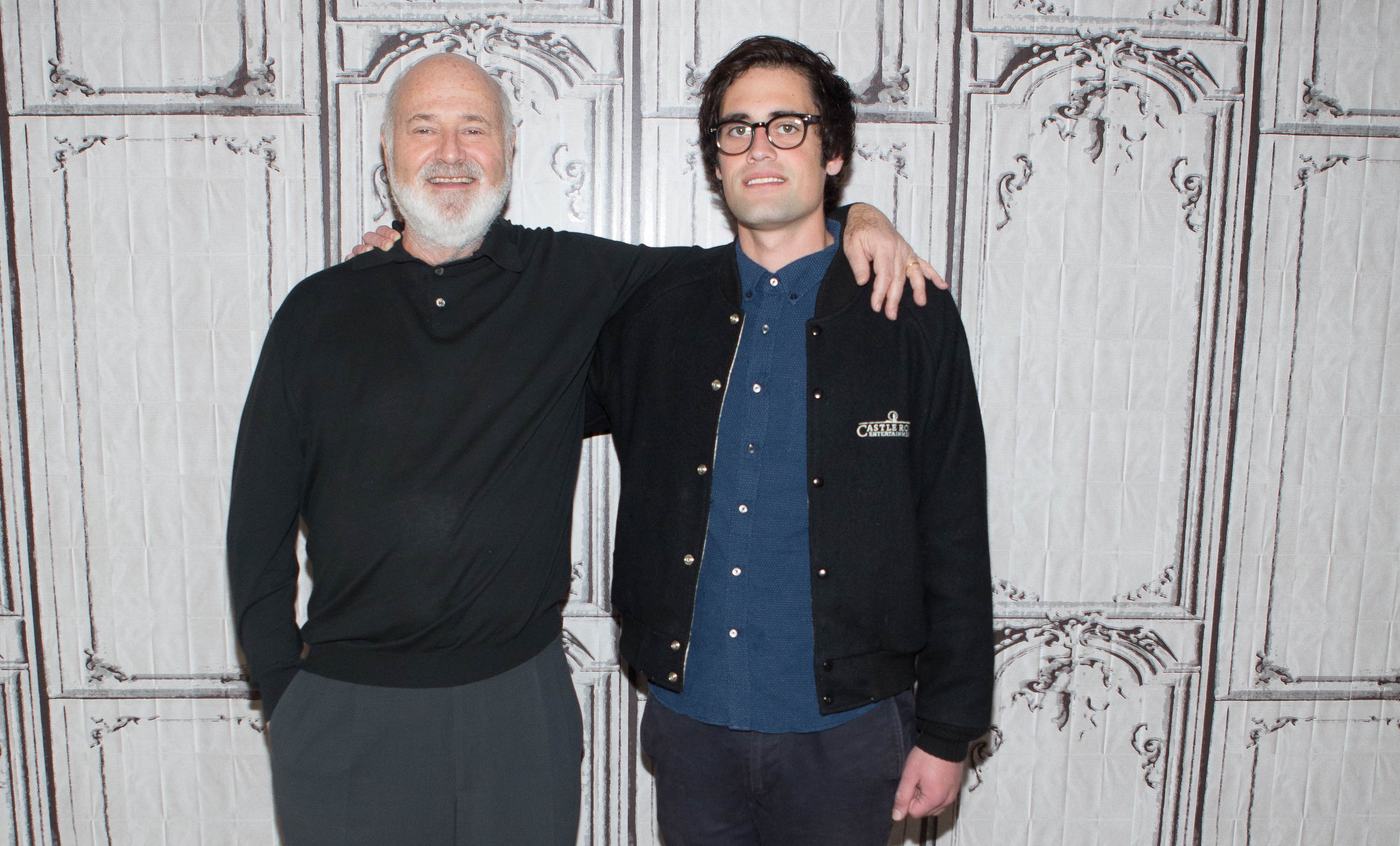 Two radical   basal   together, 1  with an limb  astir   the other's shoulder, against a decorative wall. Both are casually dressed