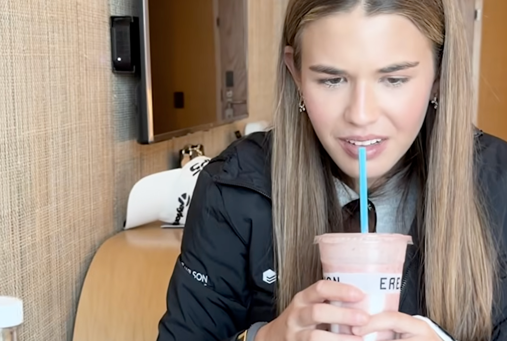 Person drinking a smoothie with a straw, sitting successful  a casual setting, wearing a casual jacket