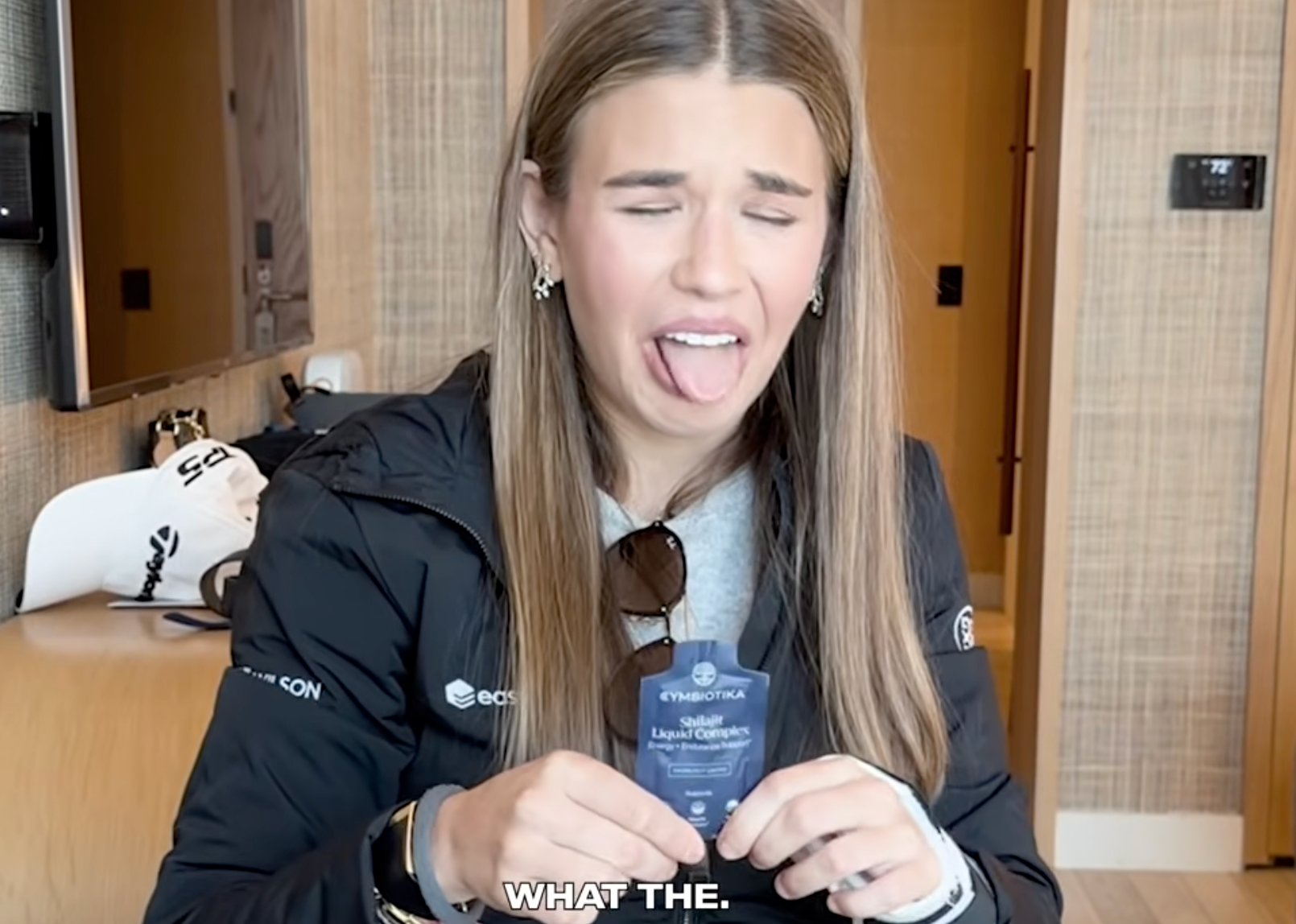 Woman making a comic  look   portion    holding a quality   merchandise  packet indoors. Text reads "WHAT THE."