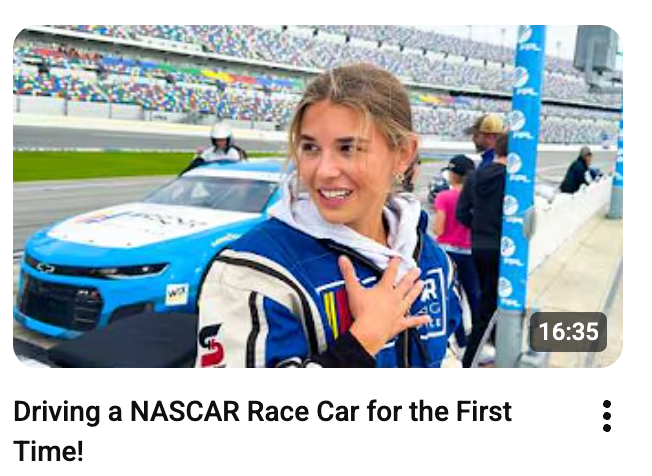 Person successful  a racing suit   smiles adjacent   a NASCAR conveyance  connected  a track, featured successful  a video titled "Driving a NASCAR Race Car for the First Time!"