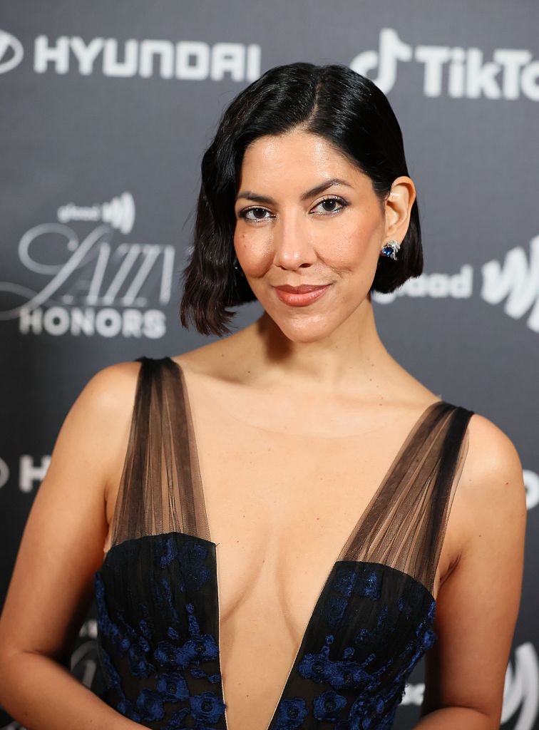 Person successful  elegant, deep-necked gown with sheer panels astatine  an lawsuit   backdrop featuring marque  logos