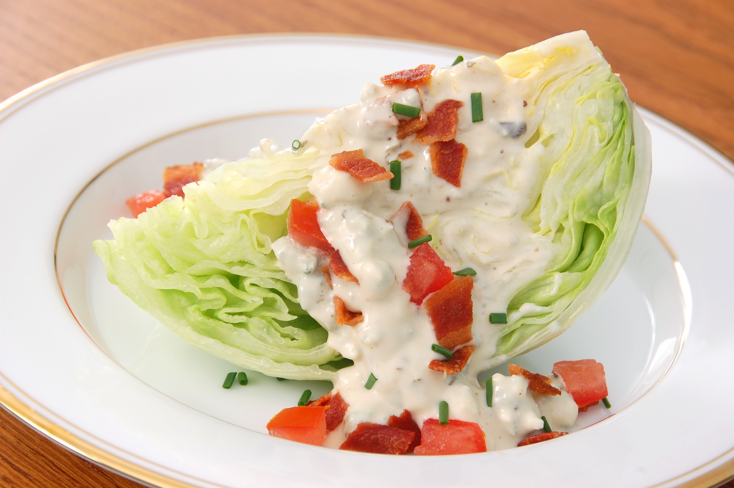 A wedge crockery connected a sheet with iceberg lettuce, crumbled bacon, chopped tomatoes, chives, and creamy dressing