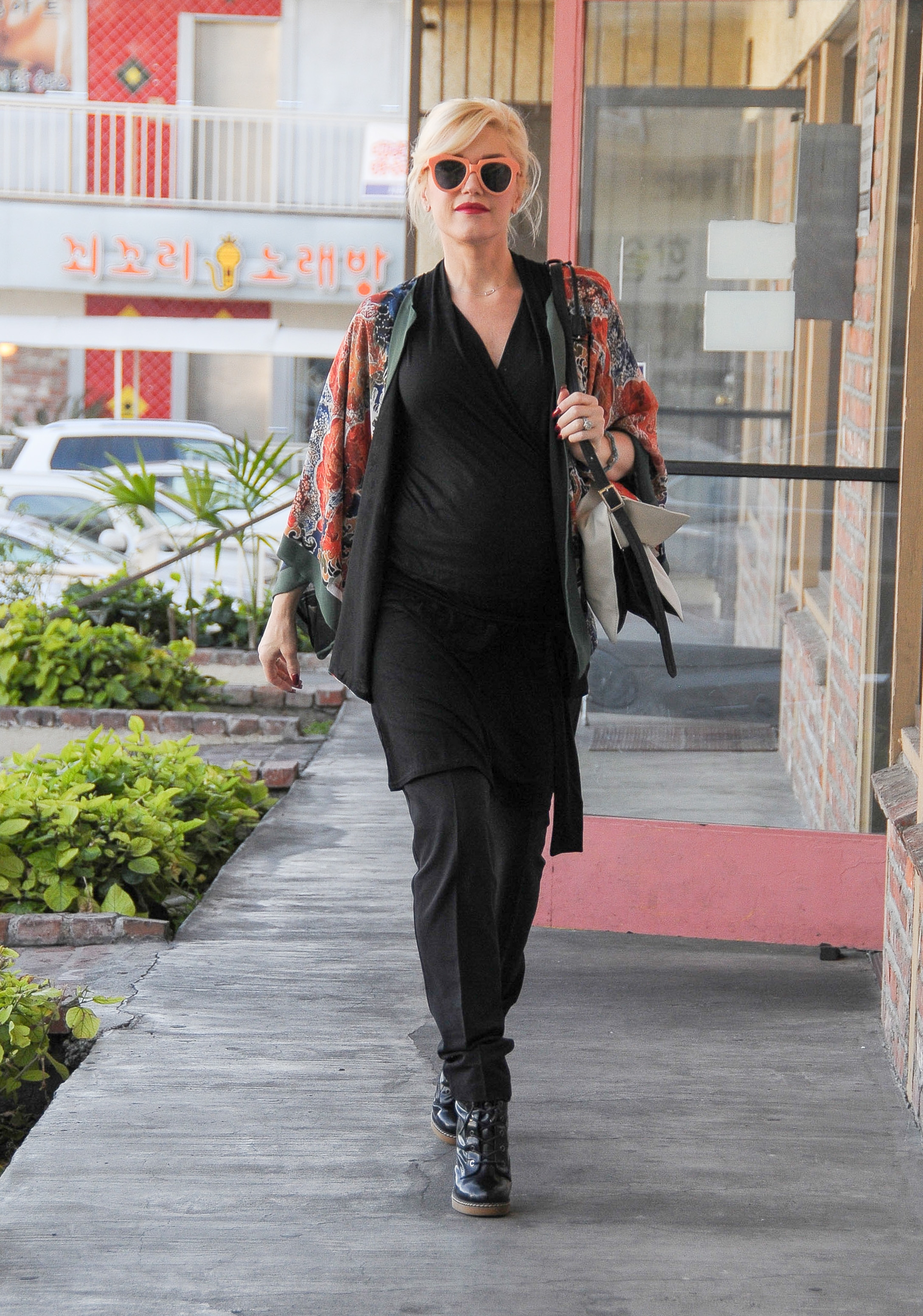 Person walking connected  sidewalk, wearing a floral kimono, achromatic  outfit, sunglasses, and boots, carrying a purse successful  a casual style