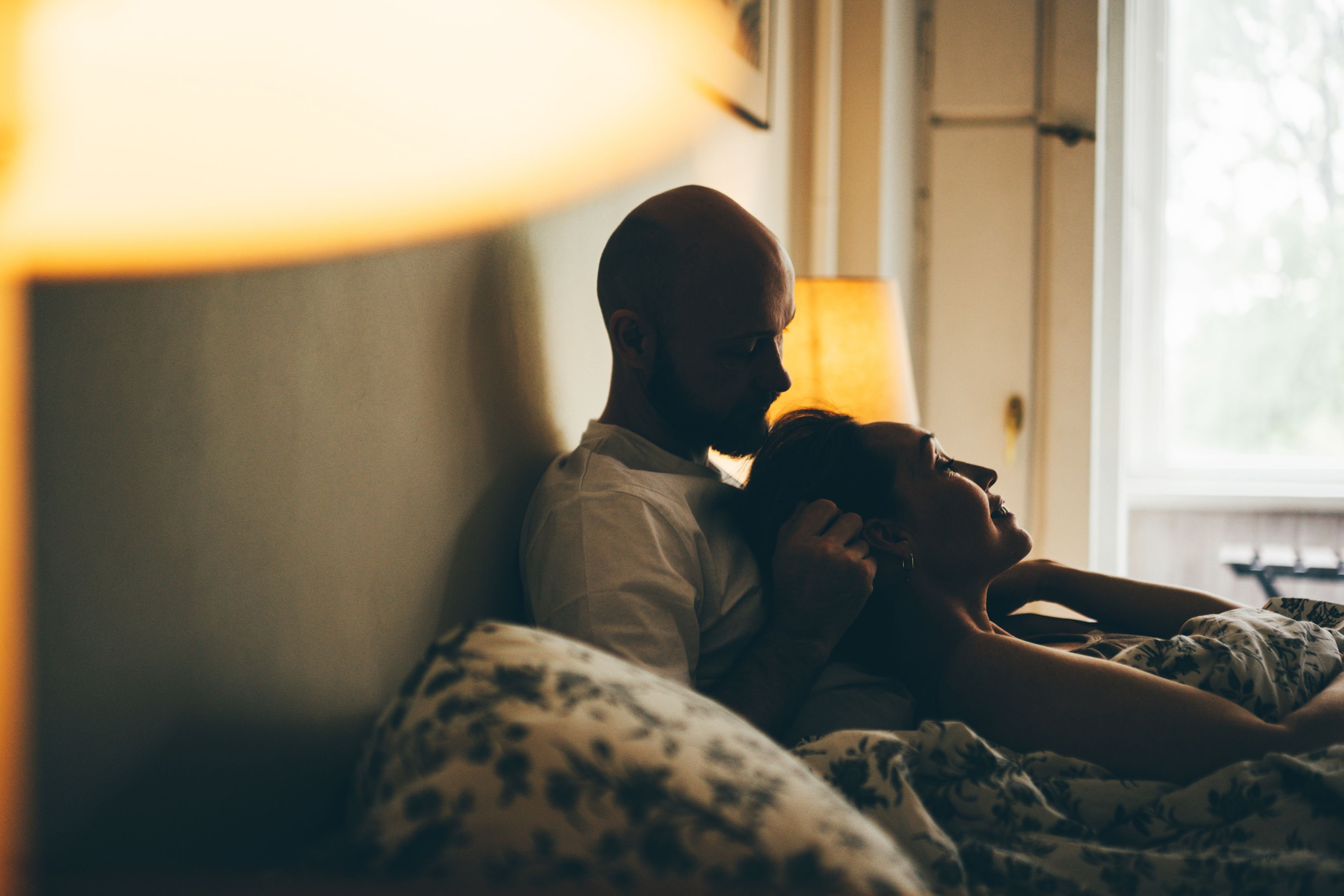 Couple cuddling in bed, lit by warm bedside lamp, enjoying an intimate moment