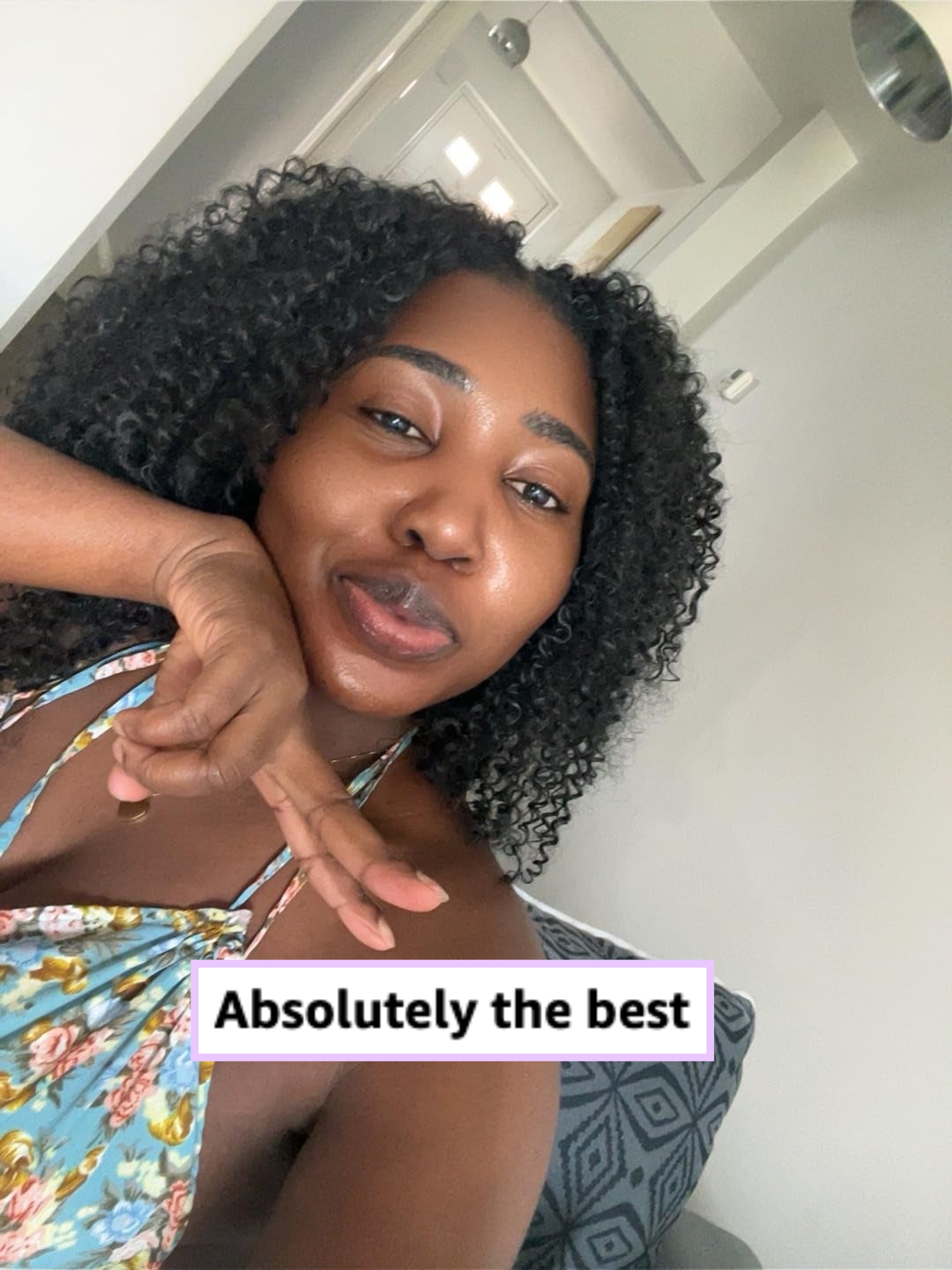 Person smiling with curly hair, wearing a floral halter top, seated connected  a patterned seat  successful  a room