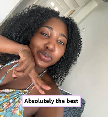 Person smiling with curly hair, wearing a floral halter top, seated connected a patterned seat successful a room