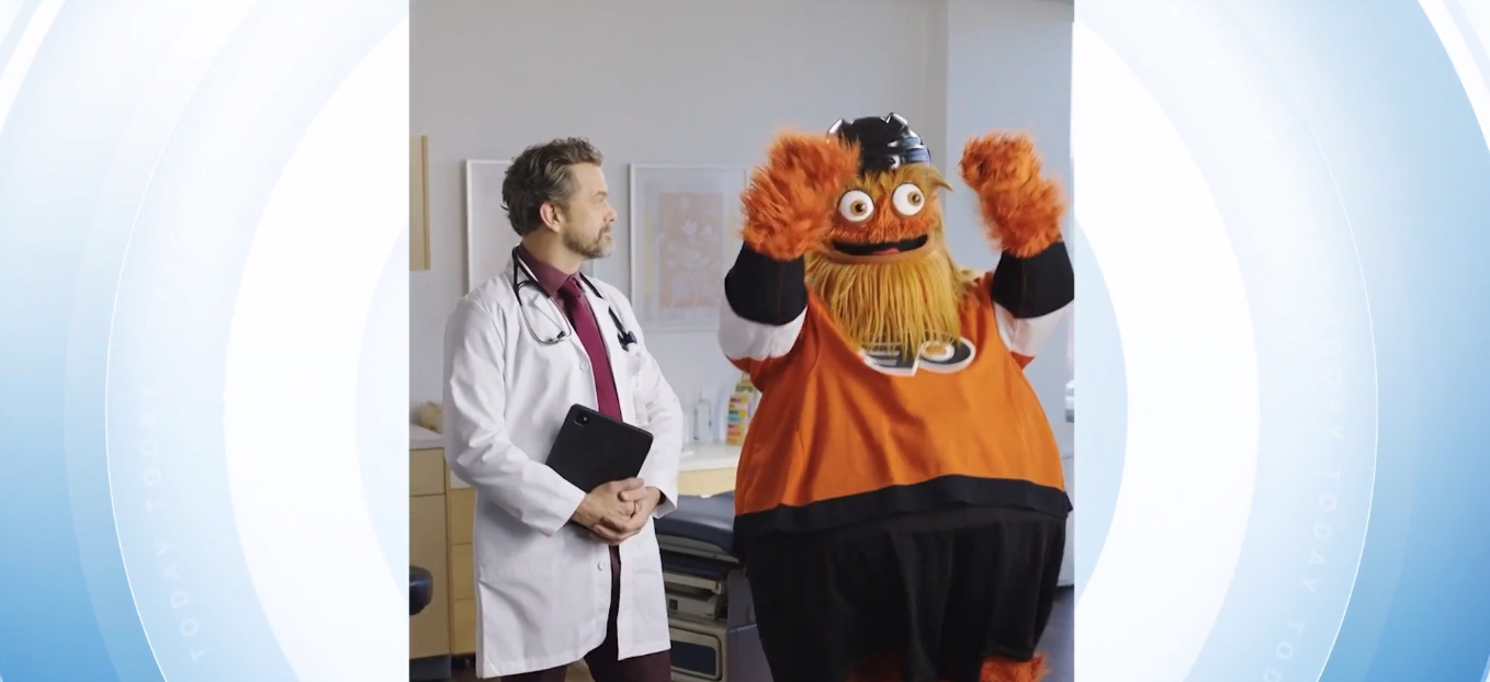 A doc  stands beside a idiosyncratic   successful  a hockey mascot costume with a bushy beard successful  a doctor's office