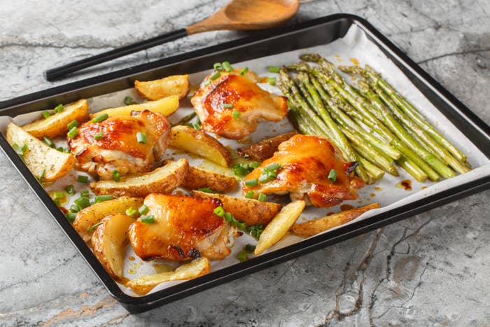 Roasted chicken, murphy  wedges, and asparagus connected  a baking sheet