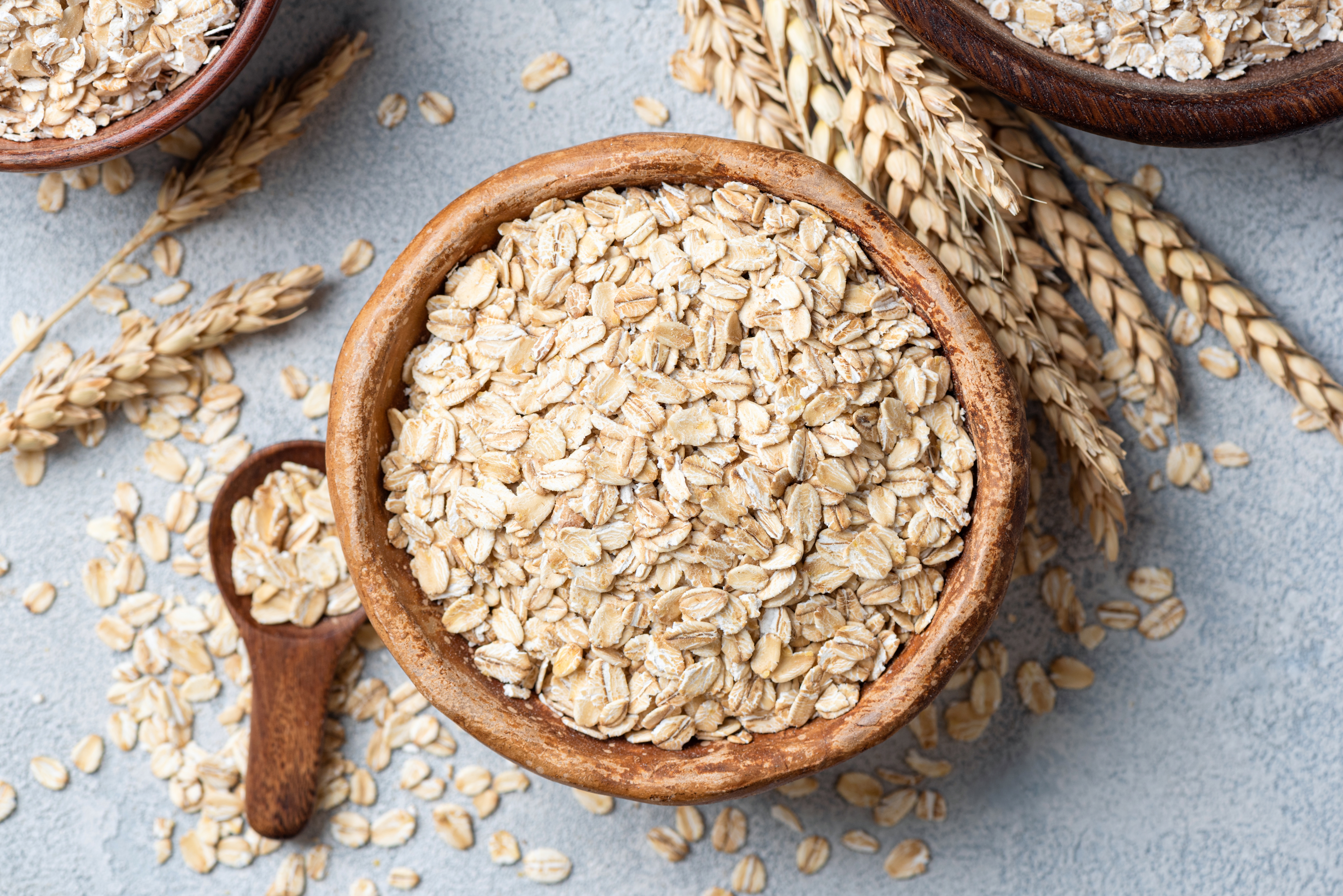 A vessel  of rolled oats with a woody  spoon connected  a textured surface, surrounded by oat stems