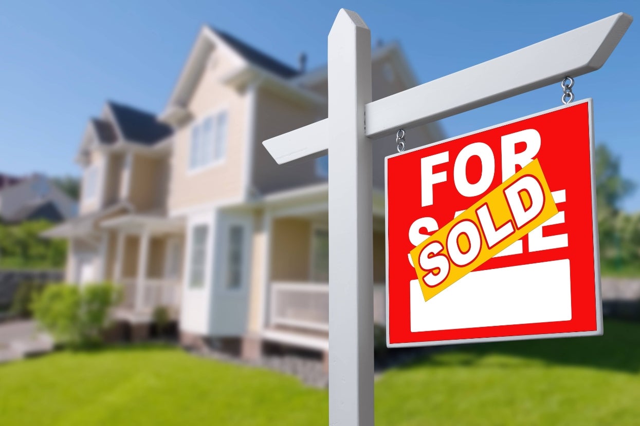 Blurred house in the background with a prominent "For Sale" sign in the foreground stamped with "Sold."