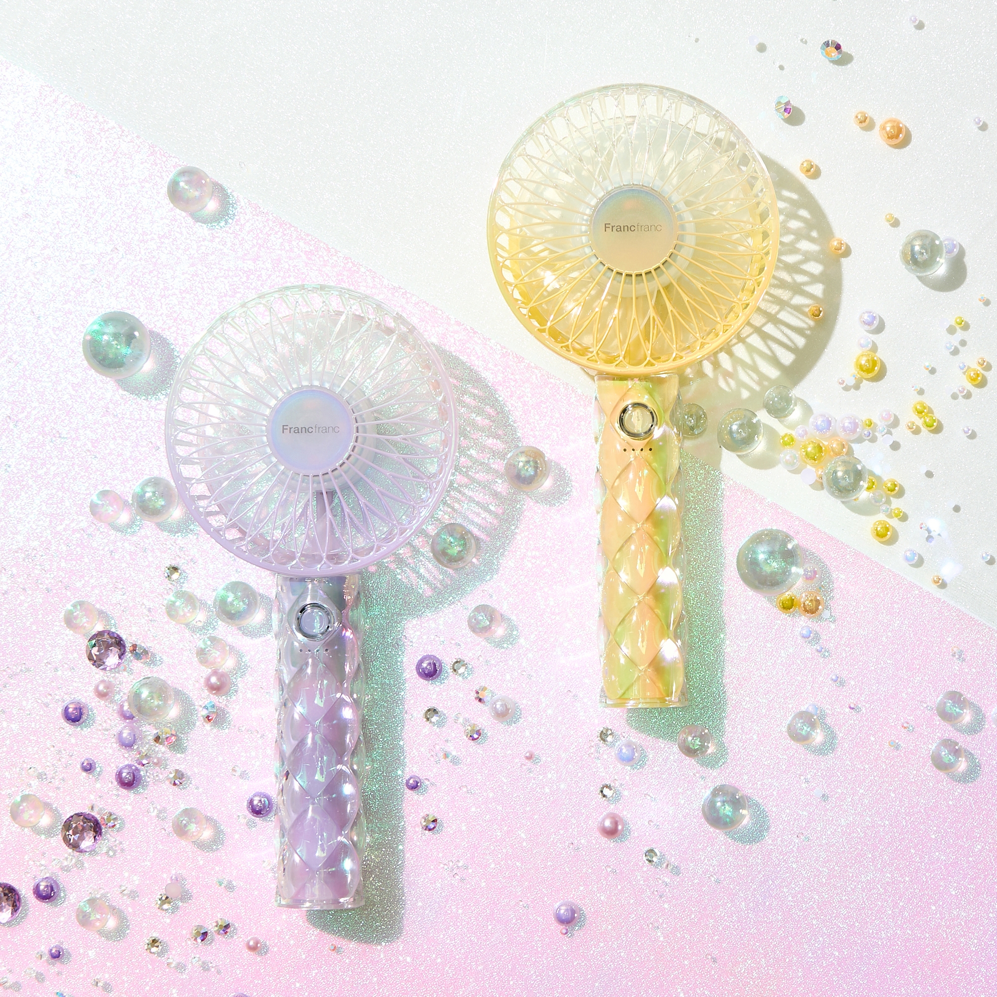 卓上に置かれた2つのフランフラン製ハンドヘルドファンが、光を受けてキラキラした背景に映えている。