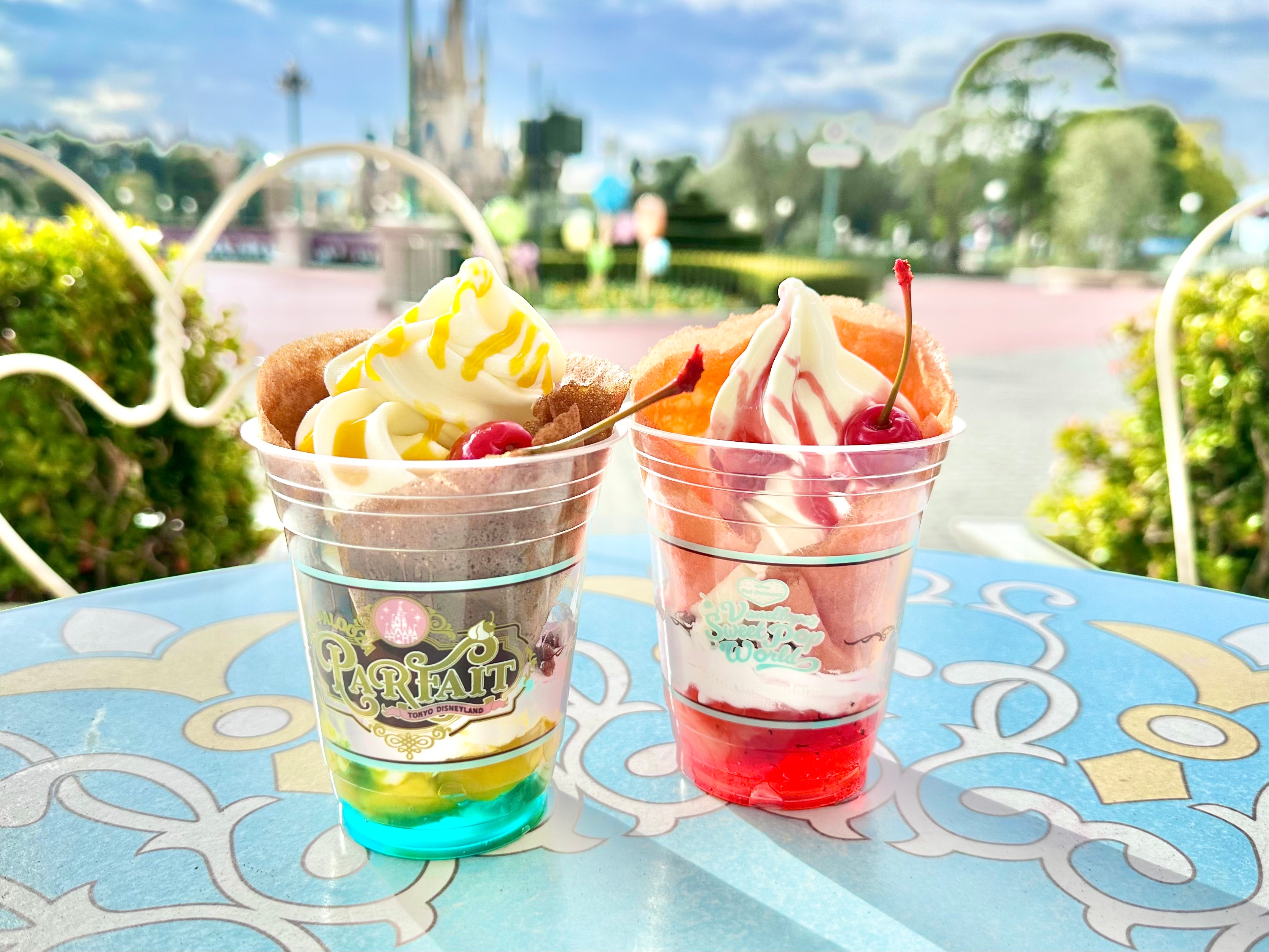 2つのパフェが屋外のテーブルに置かれ、その背景に緑の景色が広がっている。