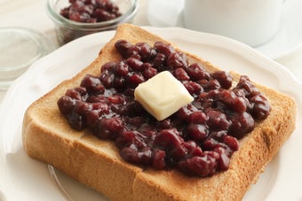 厚切りトーストにたっぷりのあんことバターがのっている。後ろにはコーヒーカップと小瓶に入ったあんこ。