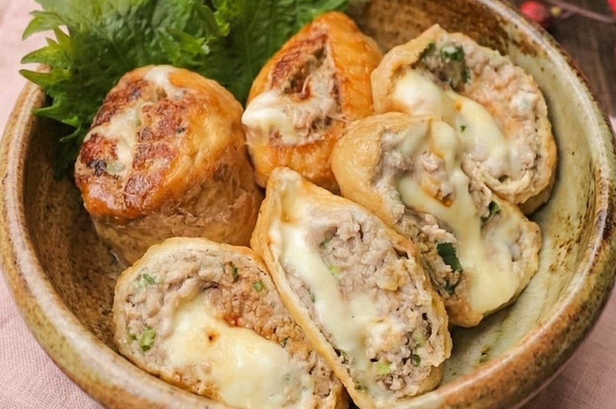 器に盛られたチーズ入り肉詰めの油揚げロール。隣にシソの葉が添えられている。