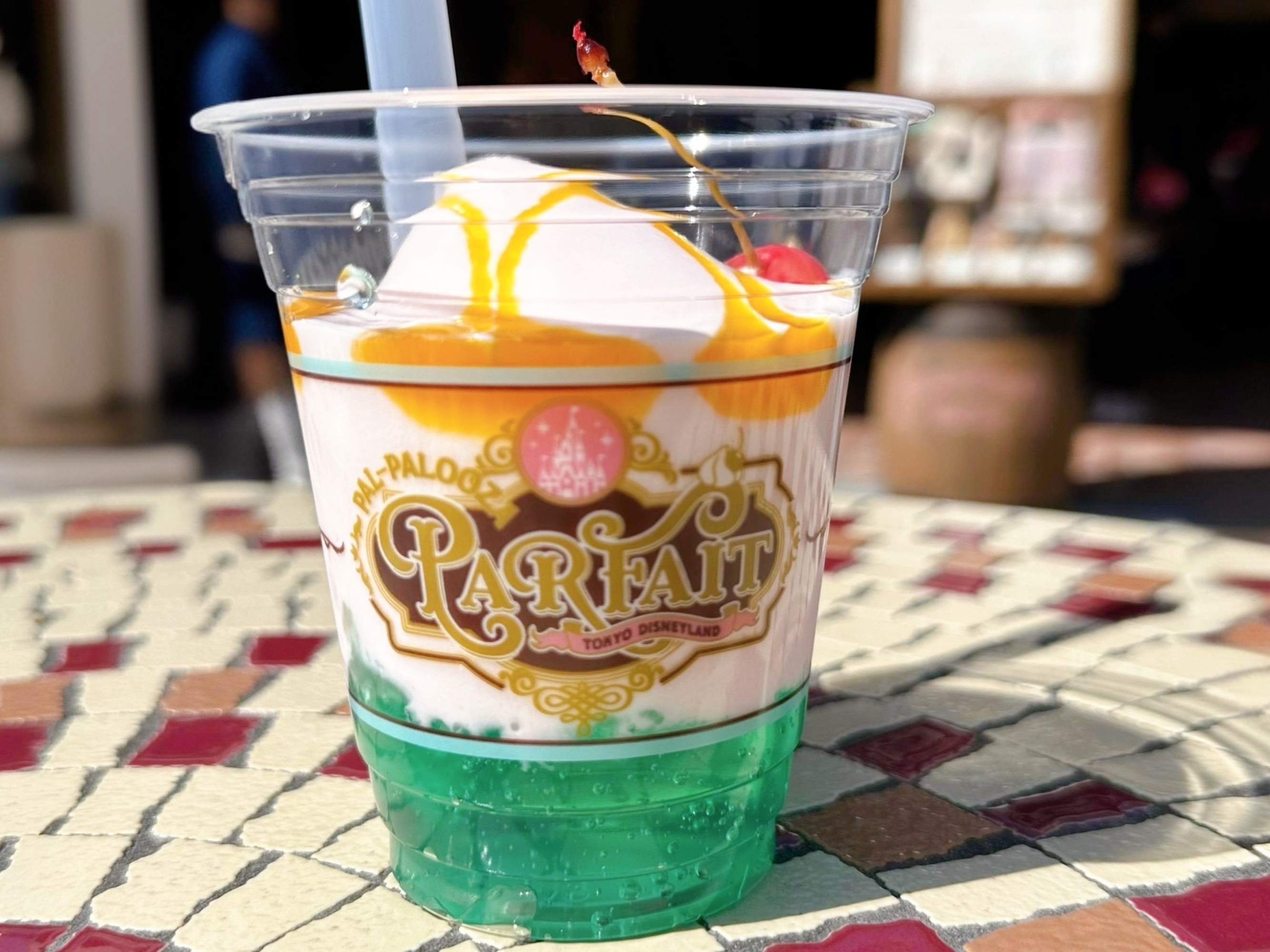 プラスチックカップに入ったパフェがテーブルに置かれている。上にソースとチェリーがトッピングされている。